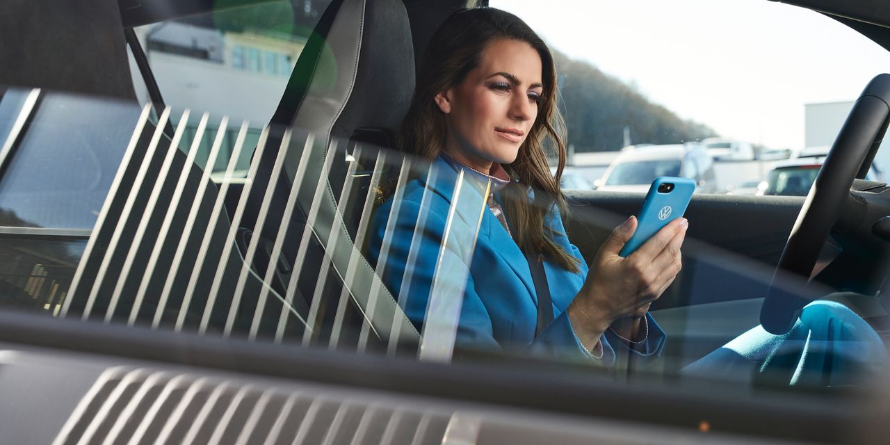 Žena oblečená v modrom sedí v zaparkovanom vozidle Volkswagen so smartfónom v ruke.