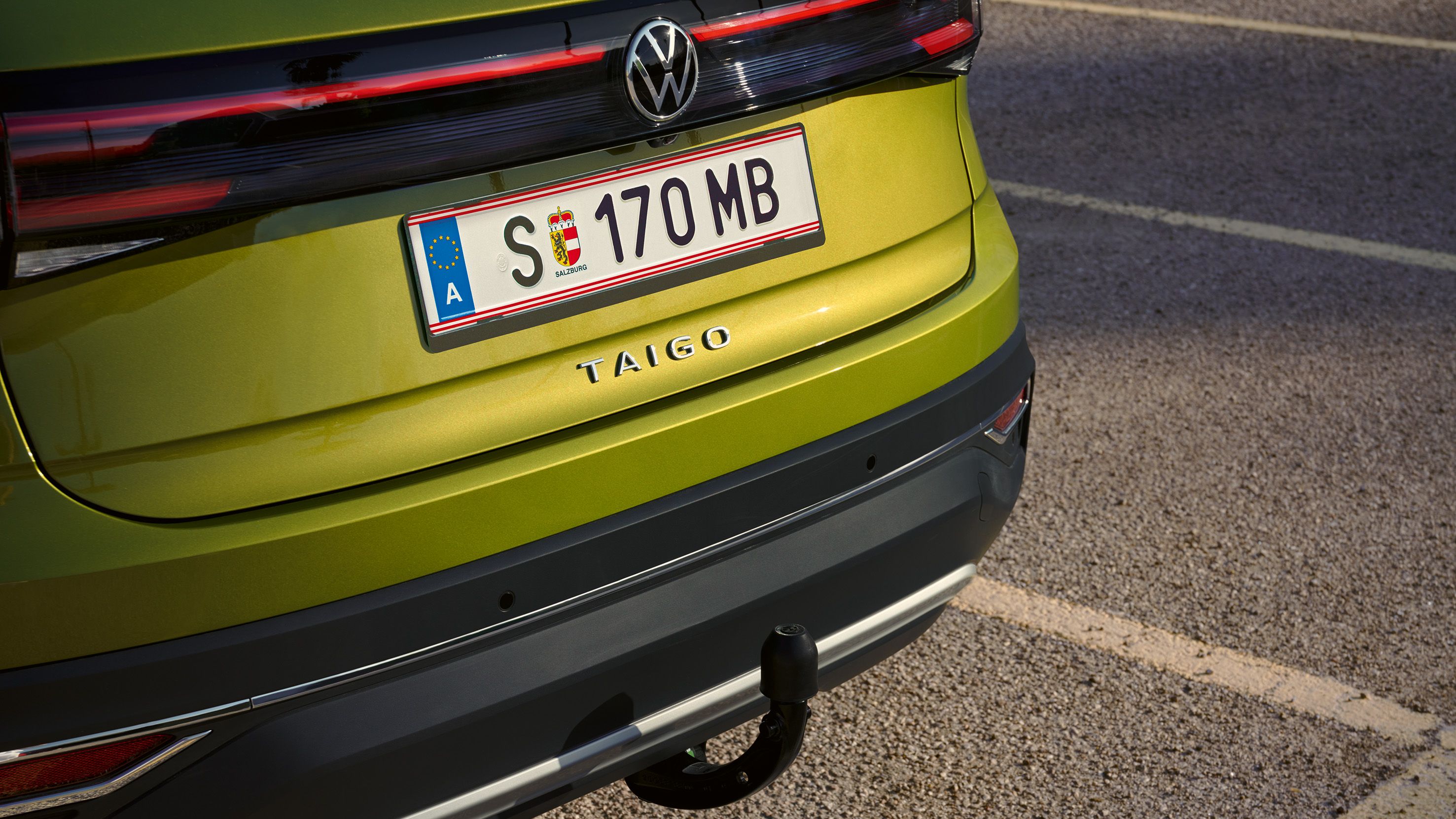 Pohľad na zadné partie zeleného VW Taigo s ťažným zariadením. Vozidlo je zaparkované na parkovacom mieste pri ceste.