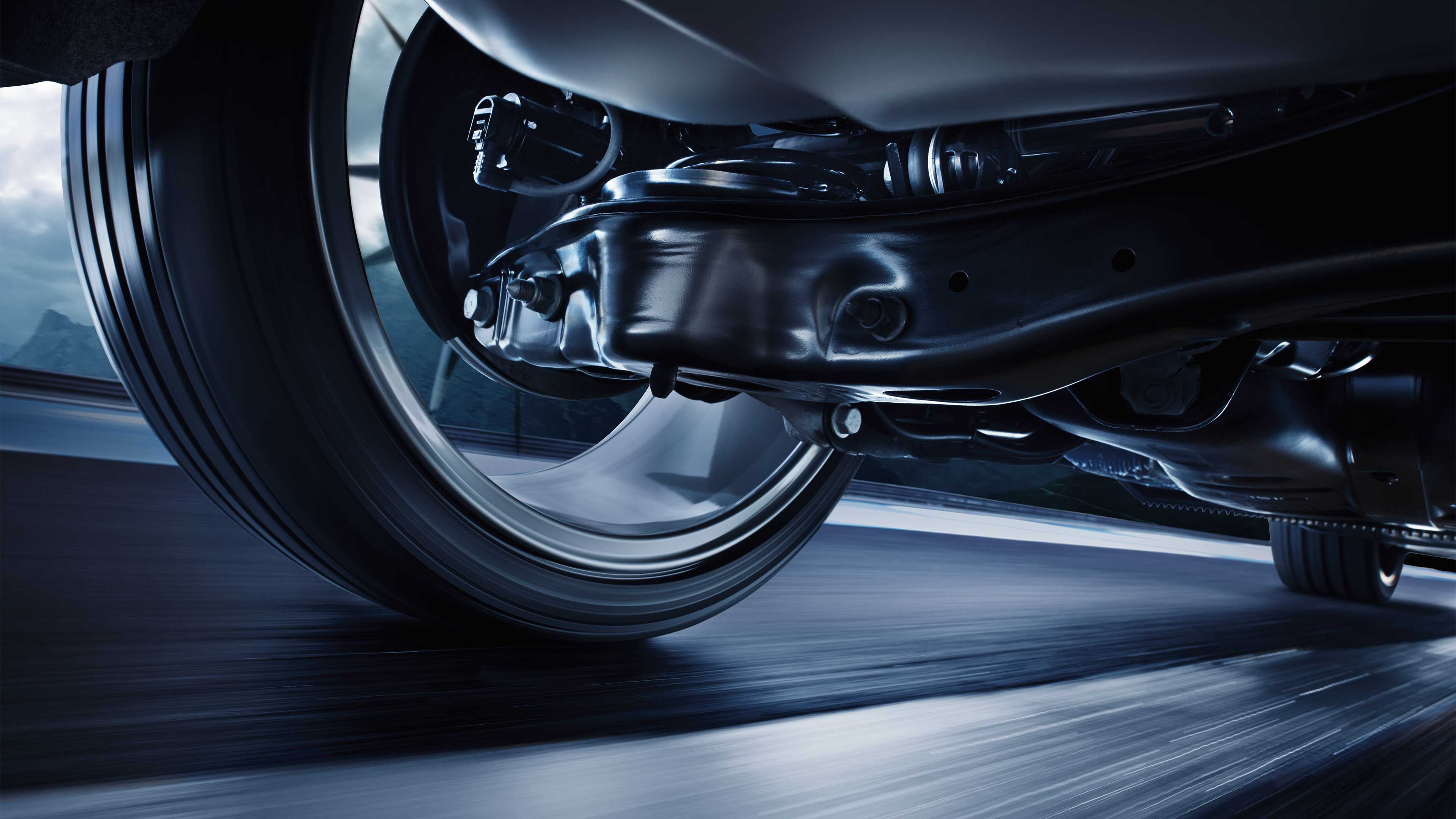 Detailný záber na podvozok automobilu počas jazdy. Viditeľná je časť zavesenia kolesa. Pozadie je rozmazané, čo vytvára dojem pohybu.