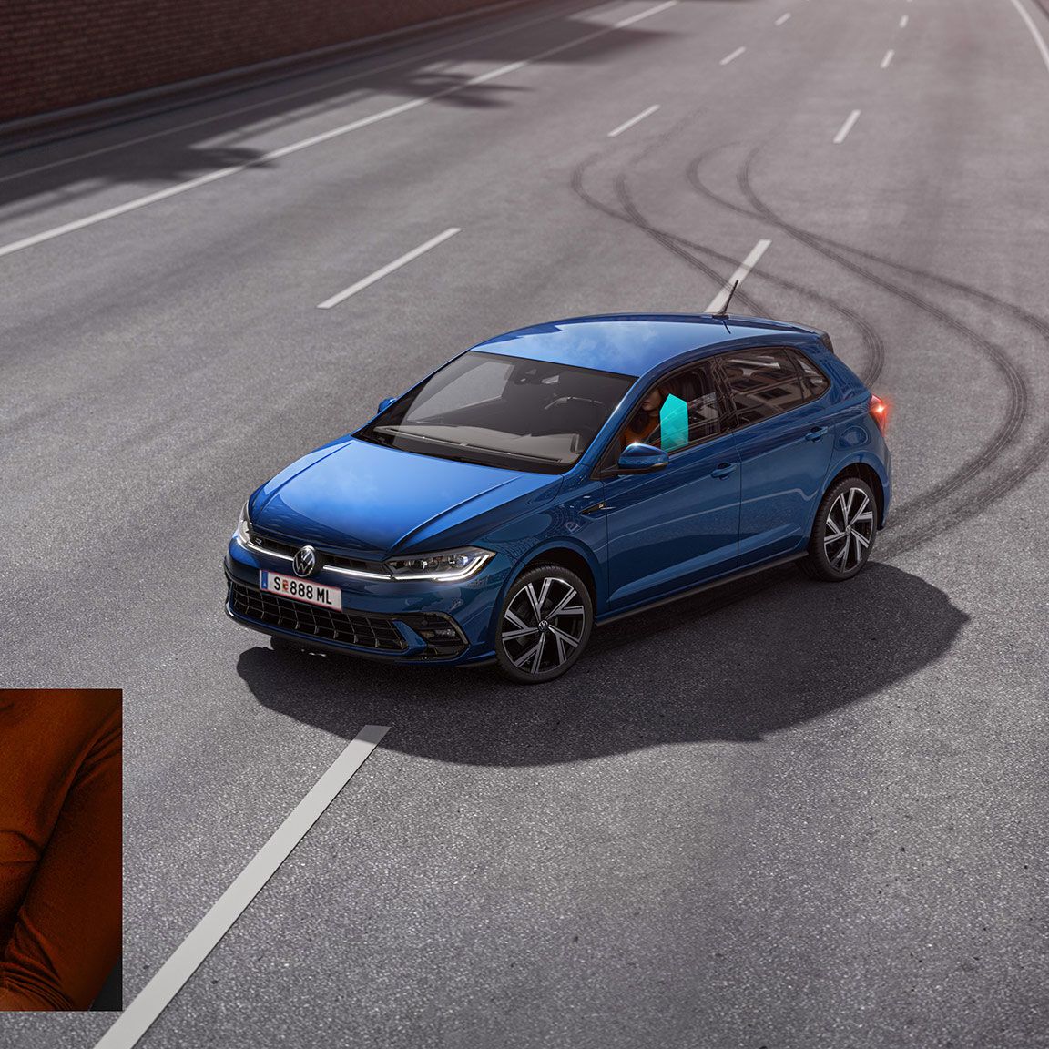 Modré auto v šmyku na prázdnej ceste, na ktorej sú viditeľné stopy po pneumatikách. V ľavom dolnom rohu je detail ruky vodiča držiace volant. Modrá šípka na okne znázorňuje jeho zatváranie.