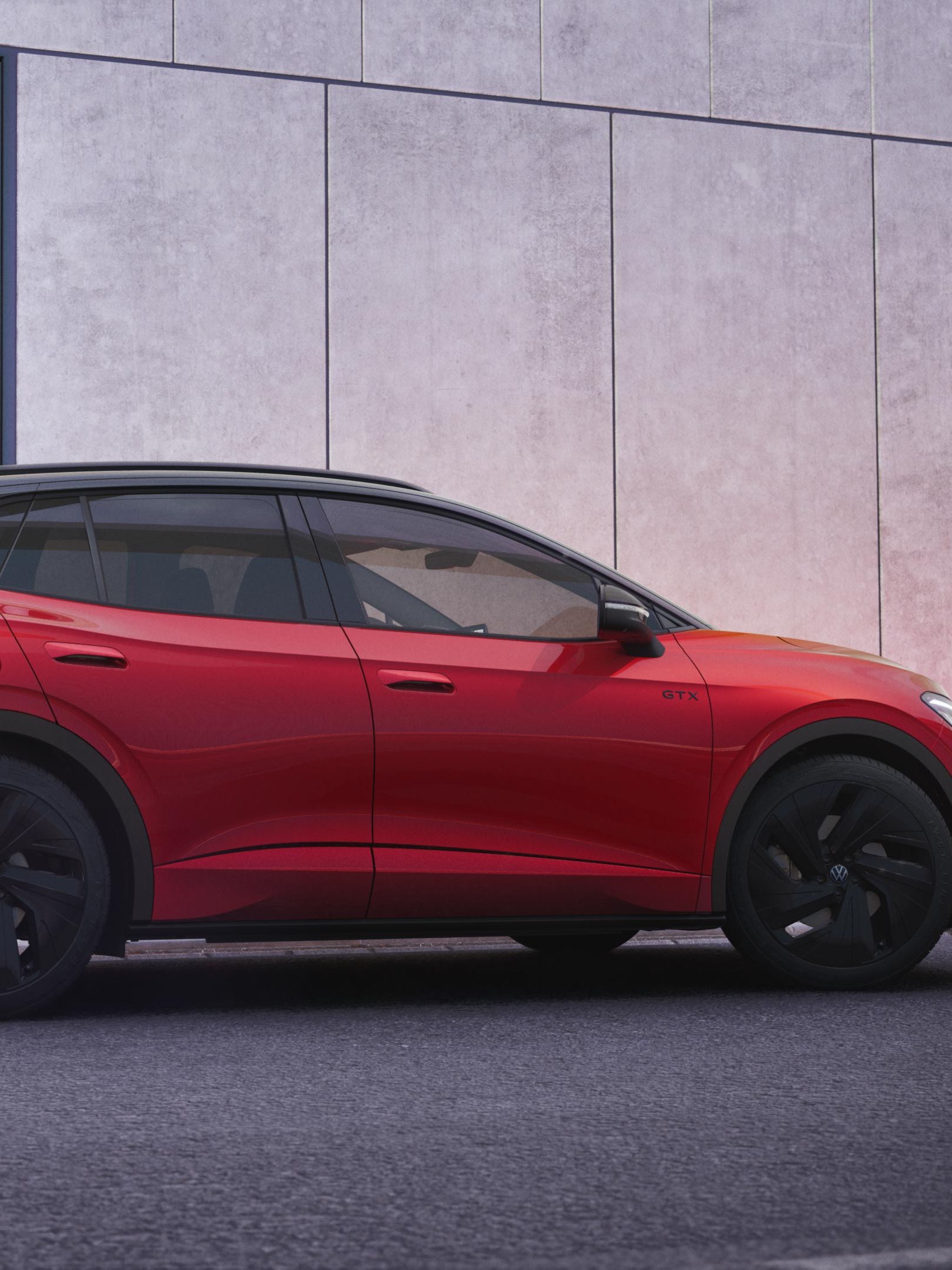 Červený VW ID.4 GTX stojí pri chodníku vedľa modernej budovy so sivou a antracitovou fasádou..