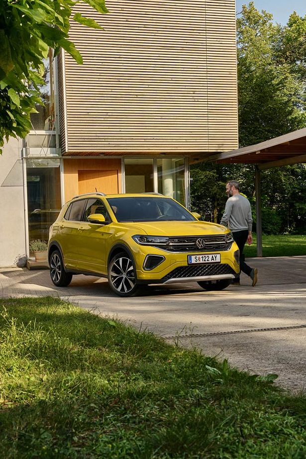 Muž sa chystá nastúpiť do žltého VW T-Cross, ktoré je zaparkované na príjazdovej ceste k domu.