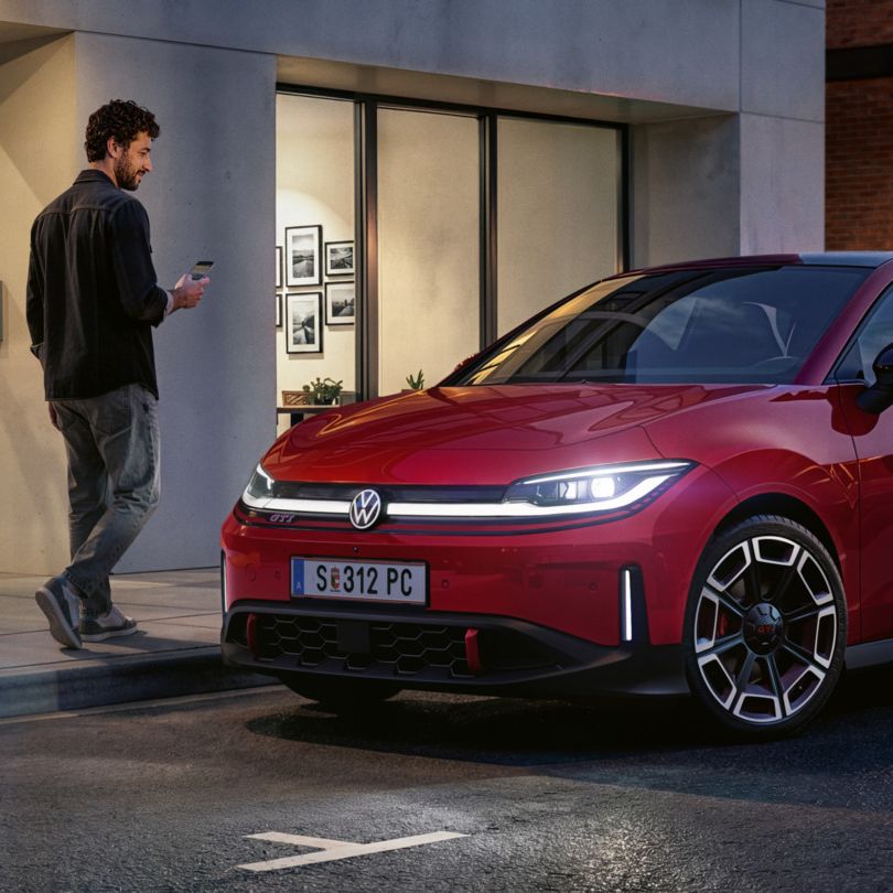 Človek prechádza okolo červeného VW ID. Polo GTI, ktoré parkuje pred modernou budovou.