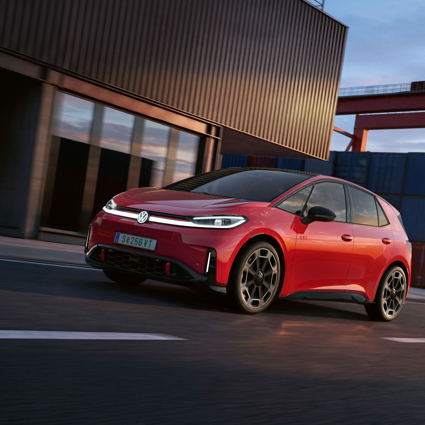 [AI-modified] – Červený VW ID.3 GTI prechádza okolo prístavnej budovy so zapnutými svetlometmi a rozsvieteným logom.
