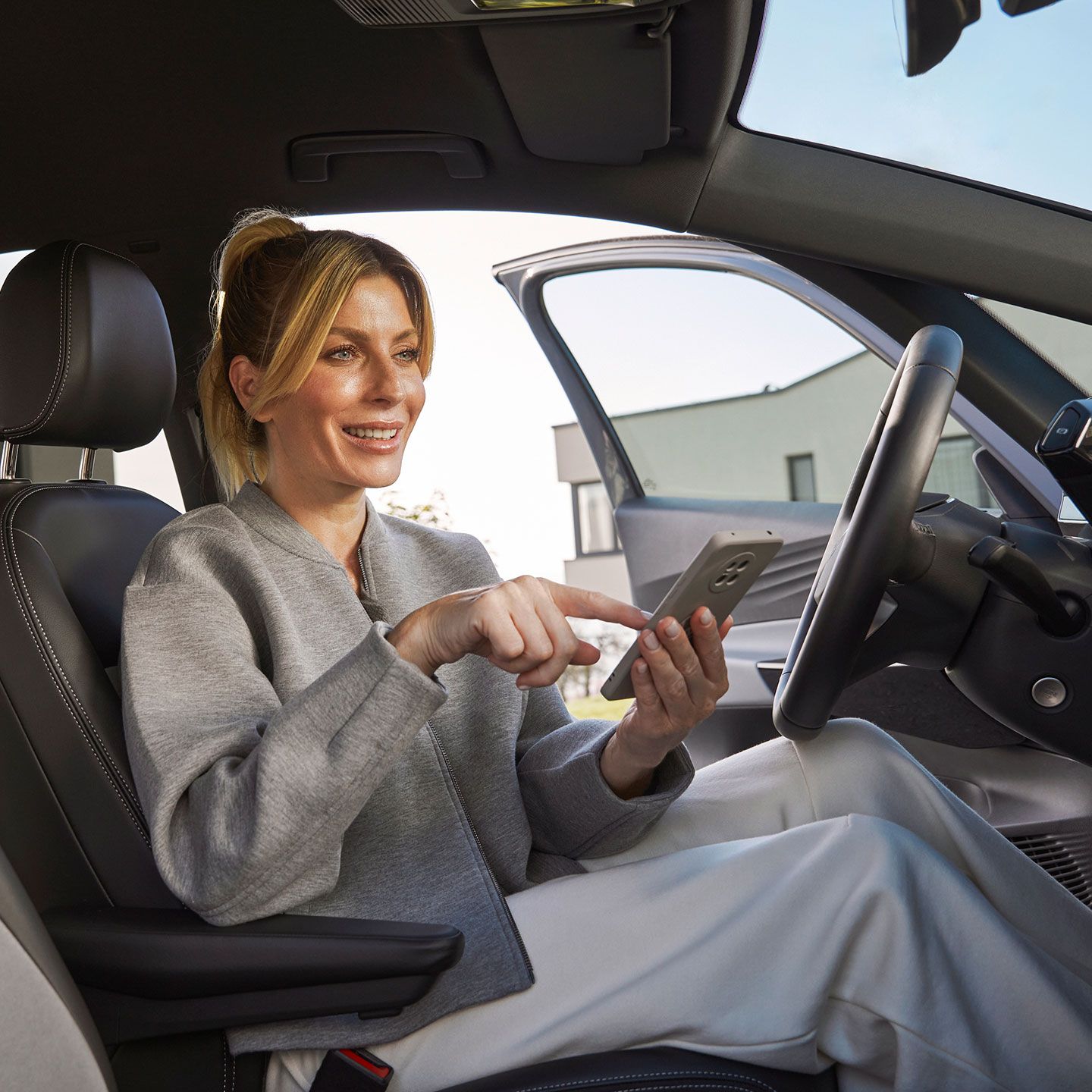 Žena sedí na sedadle vodiča vo vozidle Volkswagen a používa smartfón. Interiér auta pôsobí luxusne. 