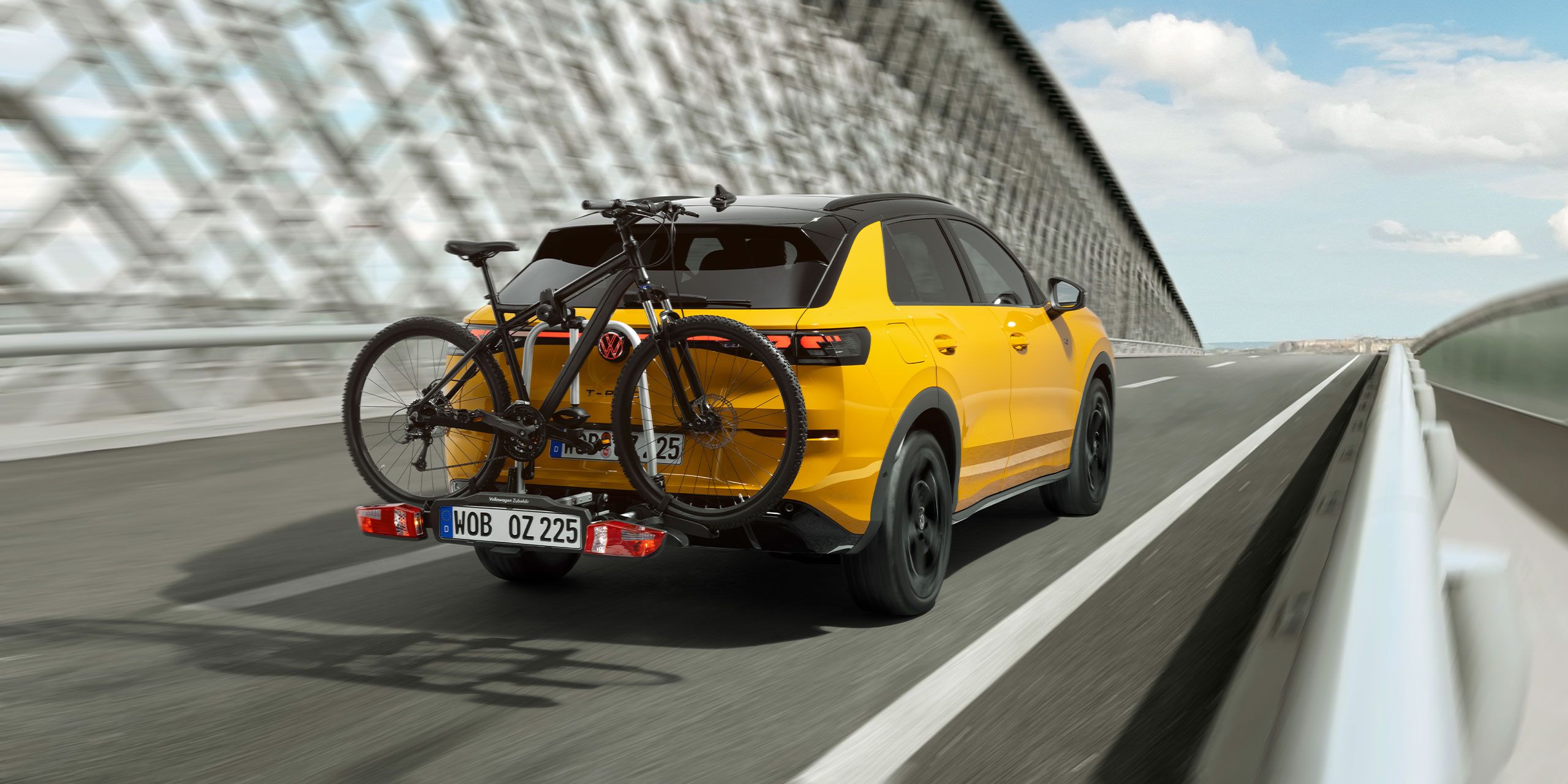VW T-Roc s nosičom bicyklov z VW príslušenstva s upevneným bicyklom jazdiaci po moste