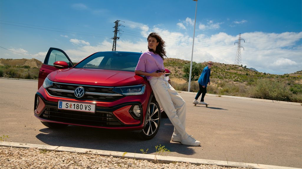 Frau lehnt an einem roten VW Taigo R-Line, dahinter ein Mann auf dem Skateboard