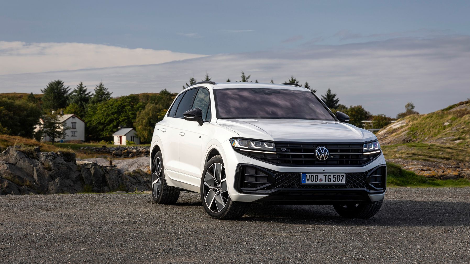Biely Volkswagen Touareg zaparkovaný na štrkovom povrchu. V pozadí vidieť domy obklopené zeleňou.