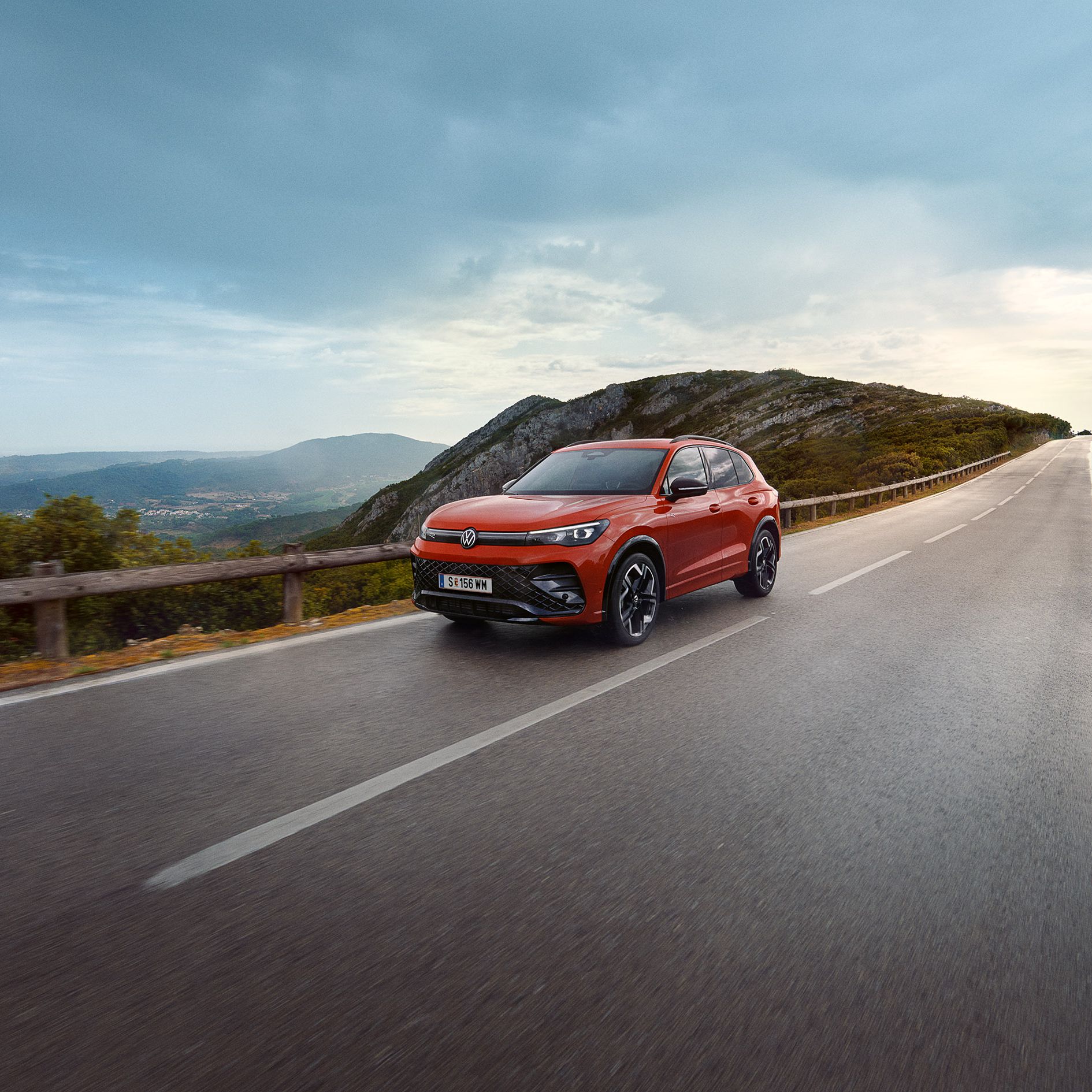 Červený VW Tiguan jazdí po ceste na horách s výhľadom do údolia.