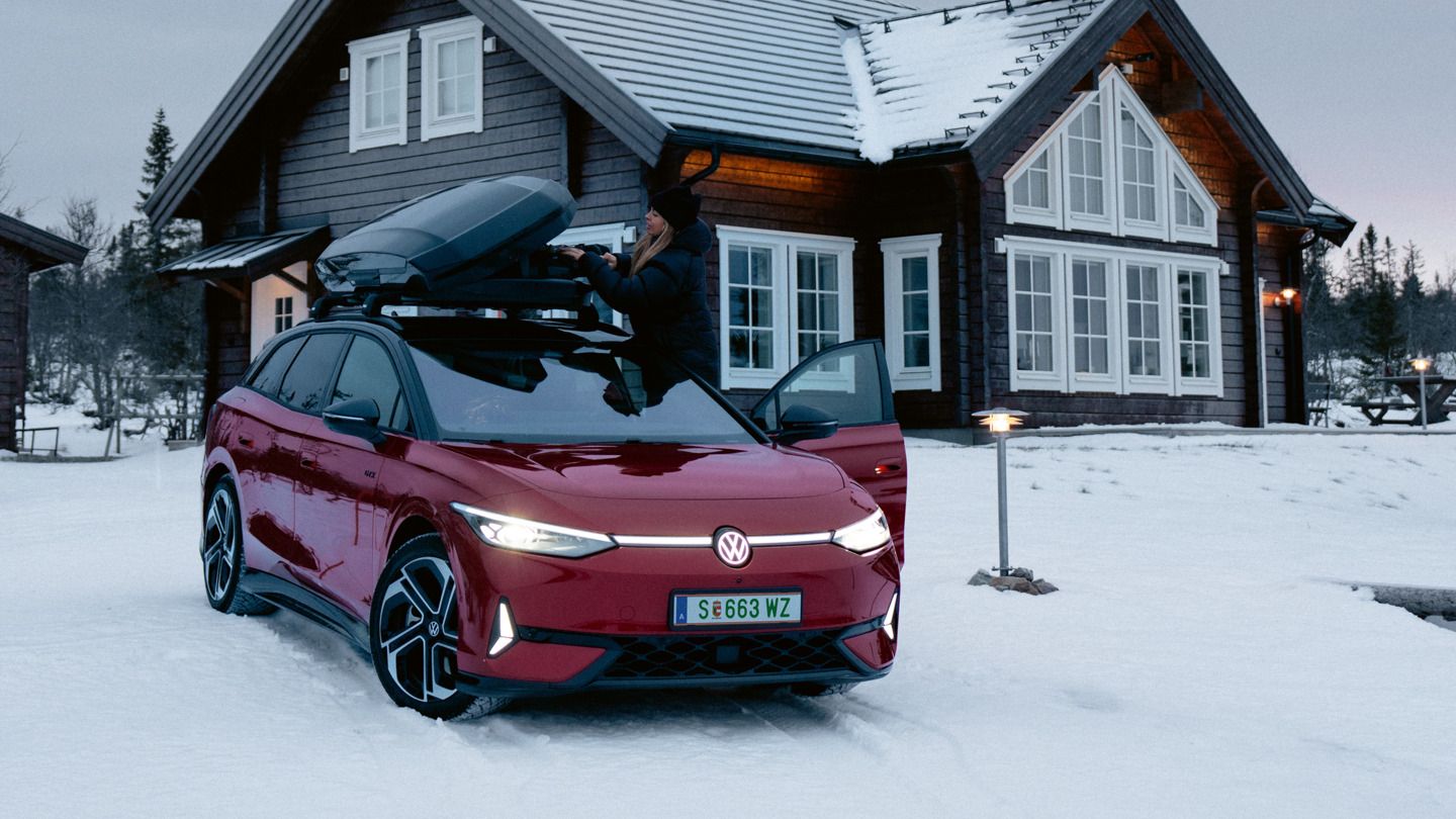 Červený ID.7 Tourer GTX so strešným boxom stojí v snehu pred domom.