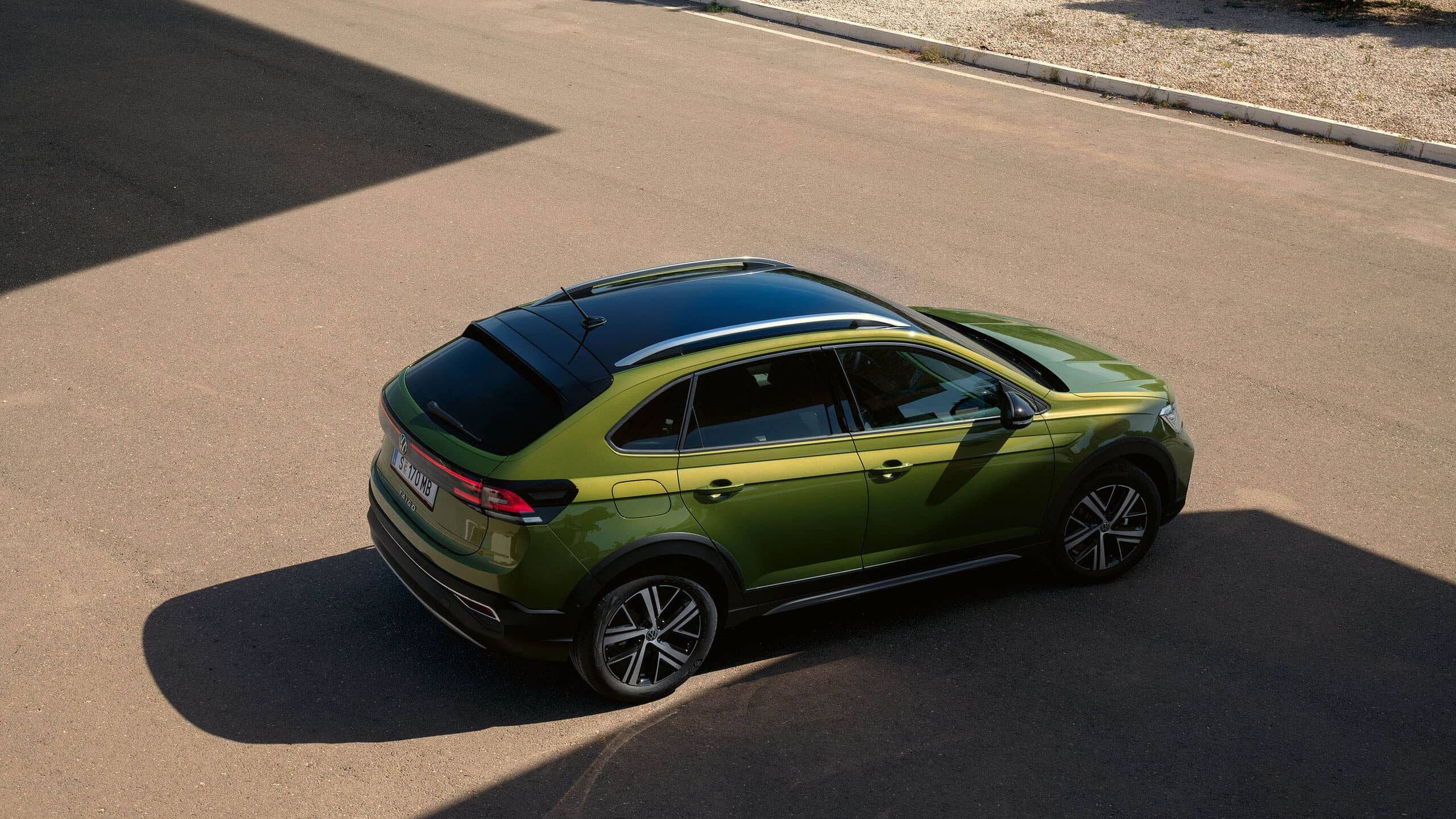 VW Taigo Style v zelenej farbe s voliteľným balíkom Roof. Pohľad na vozidlo zhora a zboku. Vozidlo stojí na voľnom parkovisku, v pozadí vidieť niekoľko stromov. 