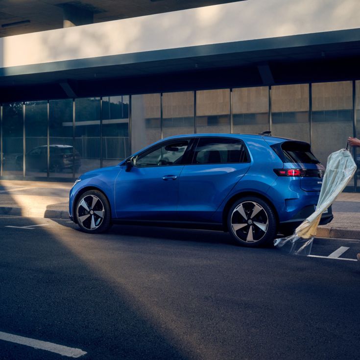 Modrý VW ID. Polo Style stojí zaparkovaný bokom pri okraji cesty, k vozidlu kráča žena.