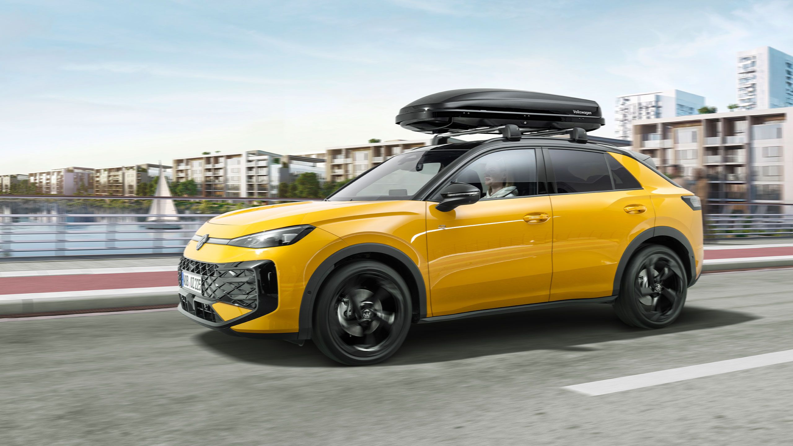 Žltý VW T-Roc so strešným boxom  idúci po ceste