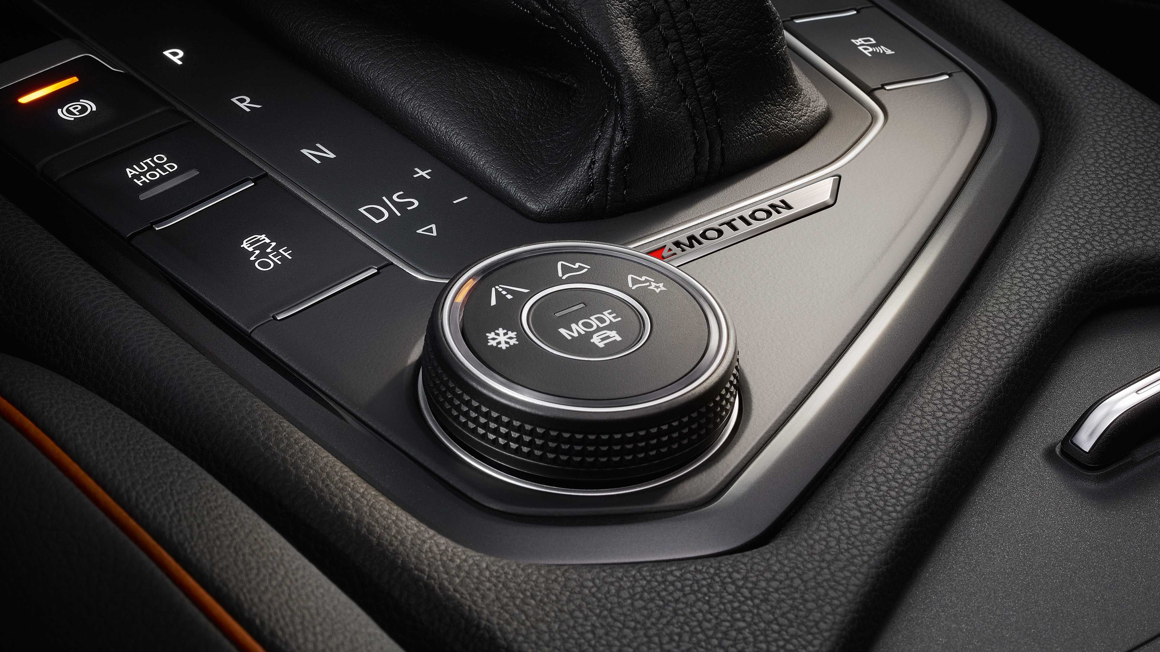 Detailný záber na ovládacie prvky automobilu vrátane otočného tlačidla s rôznymi symbolmi a nápisom "4MOTION". Viditeľné sú tlačidlá pre režim automatického módu, D/S jazdné módy a ďalšie ovládacie prvky.