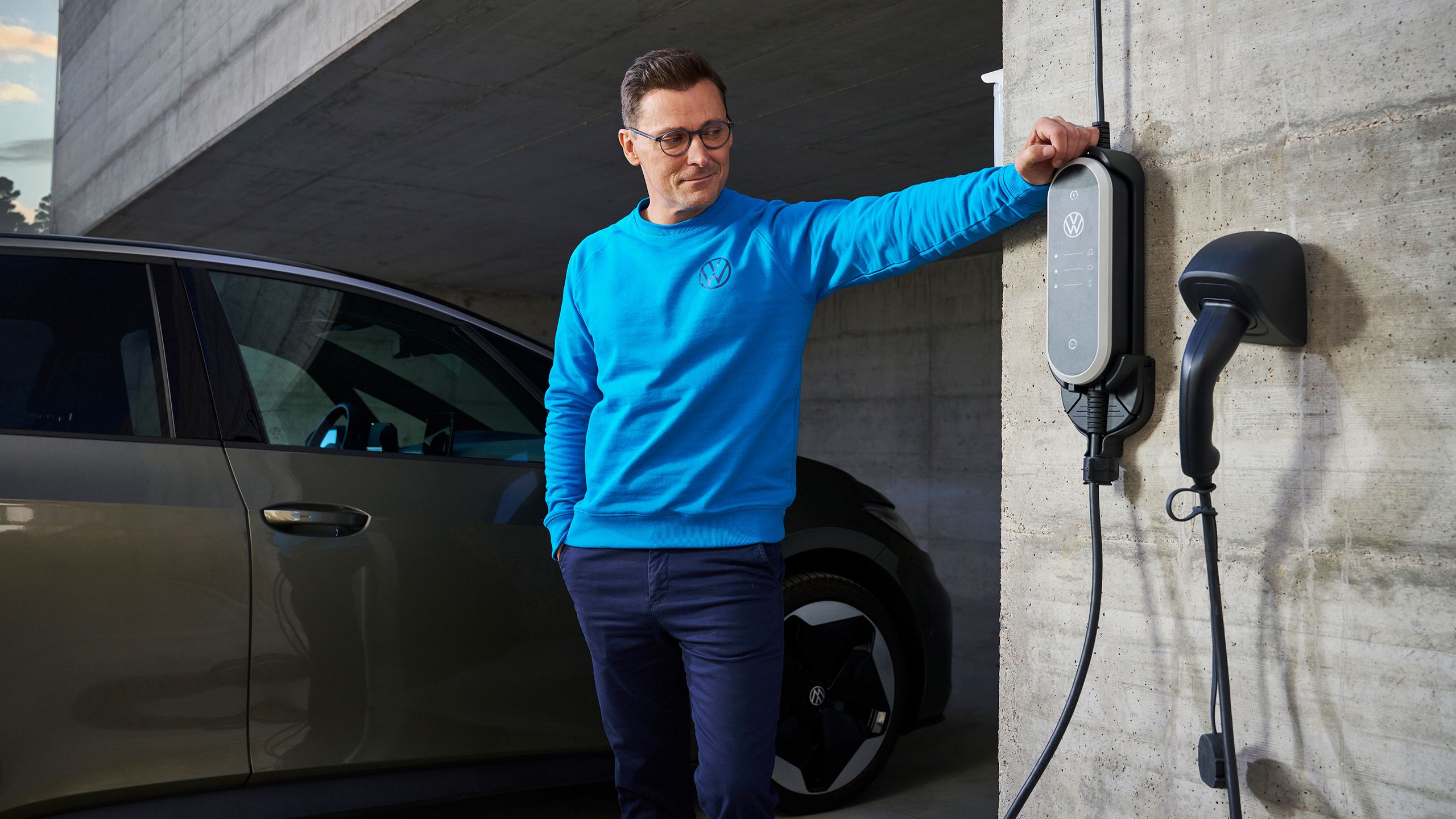 Muž stoji vedľa ID. Charger Travel z príslušenstva Volkswagen, VW ID.3 v pozadí