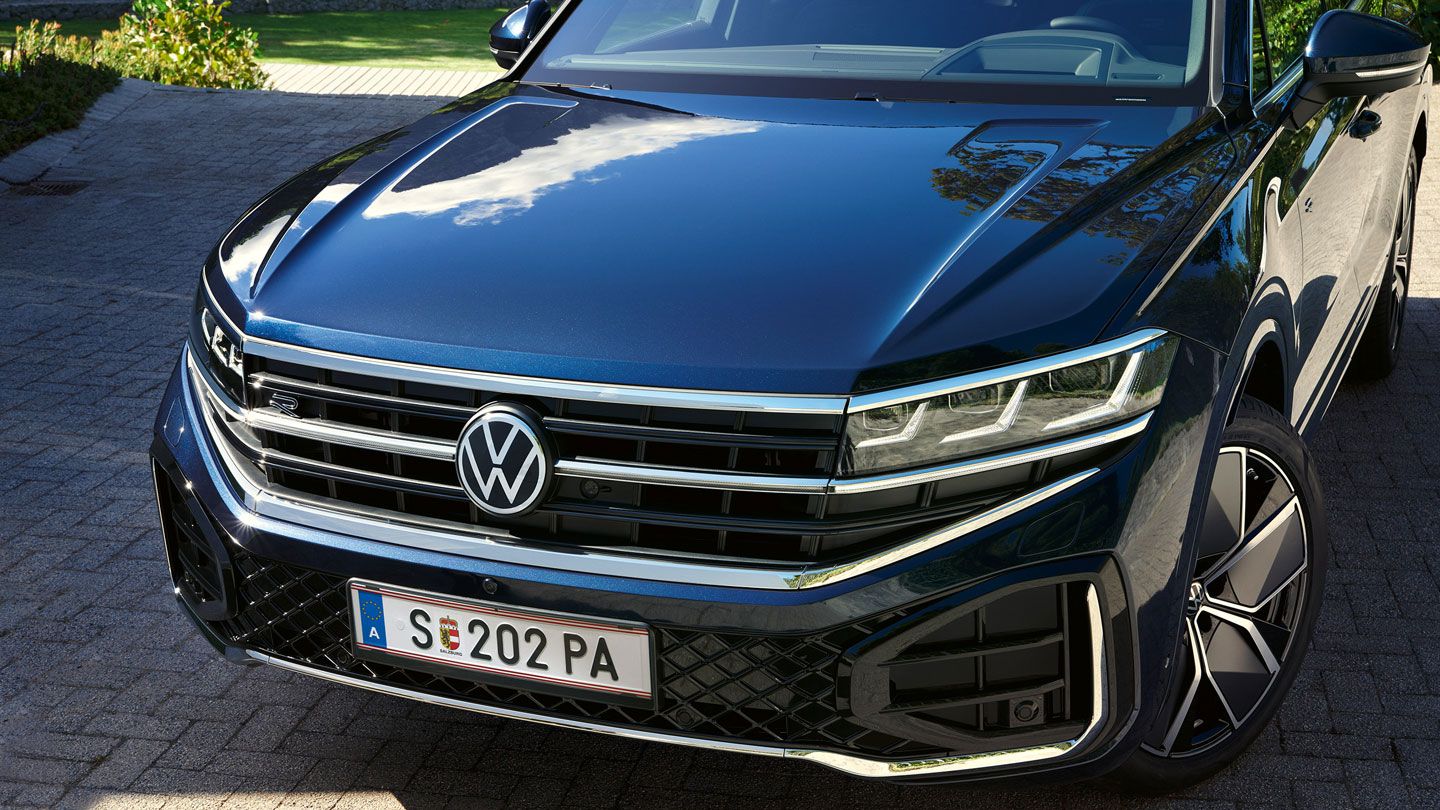 Pohľad na predné partie VW Touareg R-Line s HD Matrix LED svetlometmi. Vozidlo stojí na príjazdovej ceste lemovanou zeleňou.