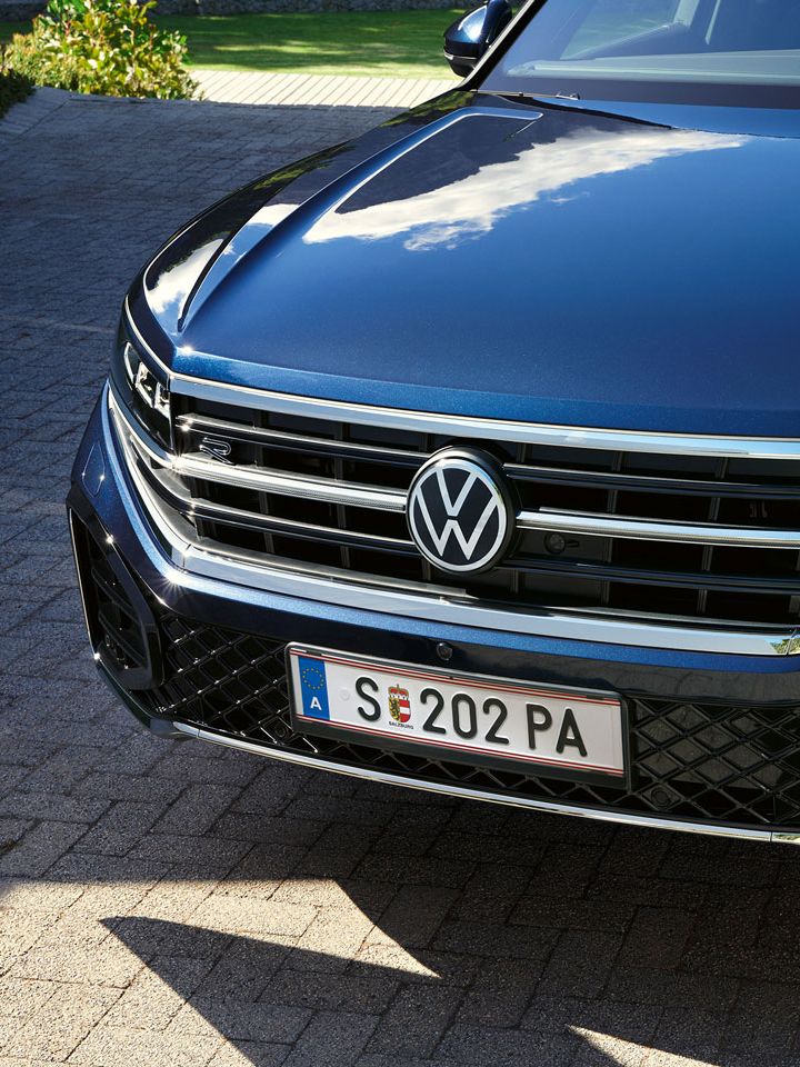 Pohľad na predné partie VW Touareg R-Line s HD Matrix LED svetlometmi. Vozidlo stojí na príjazdovej ceste lemovanou zeleňou.
