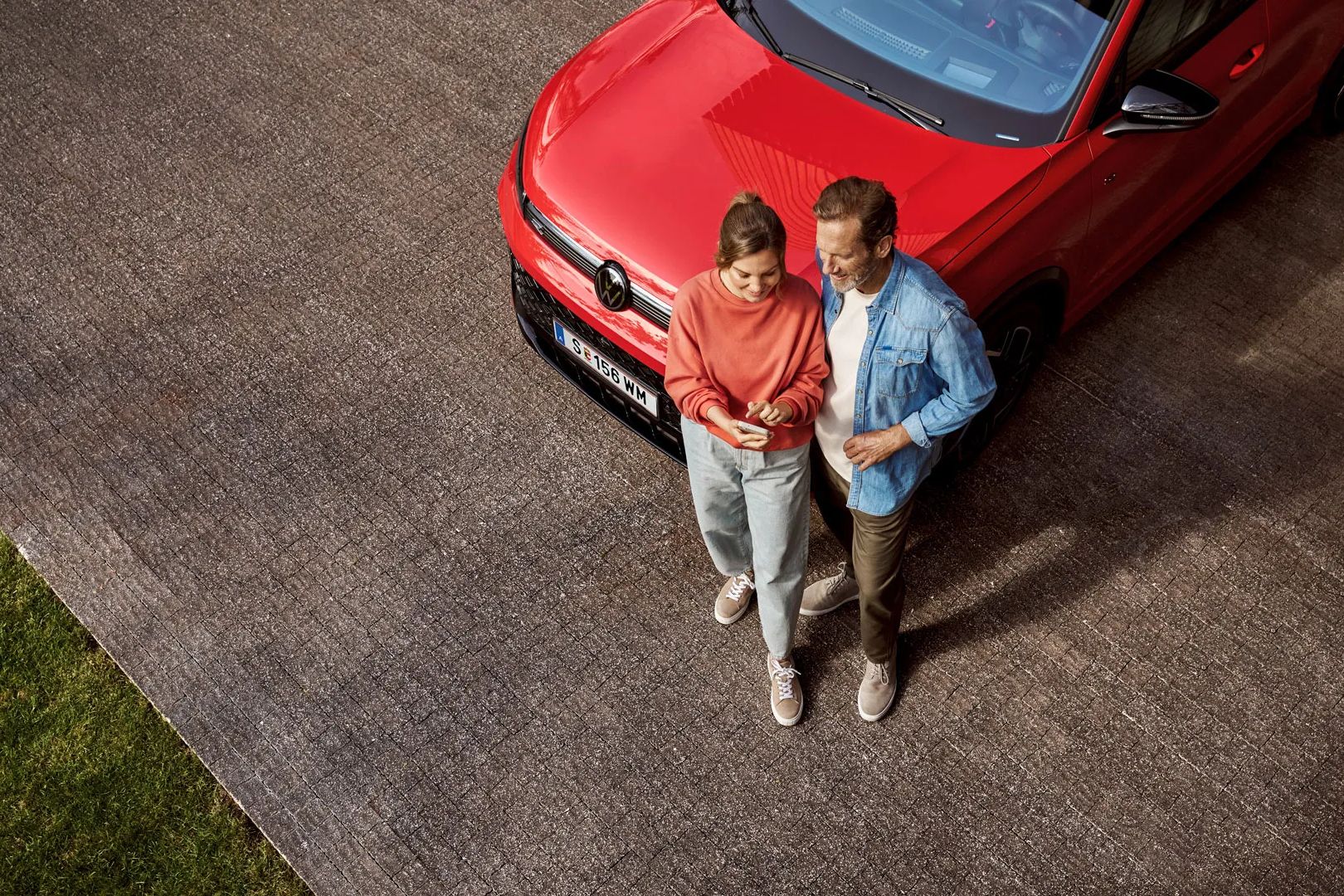 Žena a muž stoja pred vozidlom Tiguan a spolu sa pozerajú na mobilný telefón. Vozidlo je zaparkované na ceste.