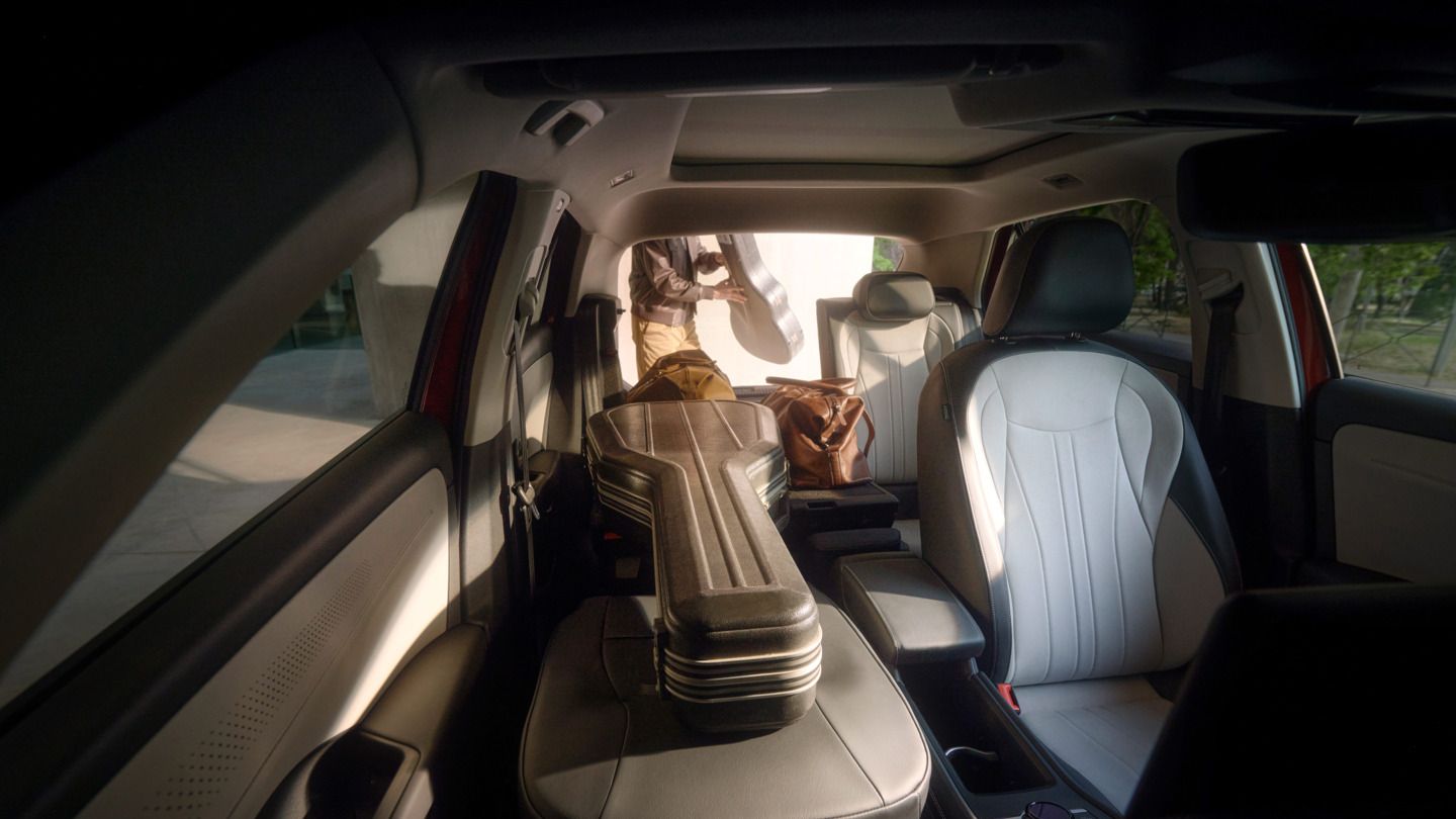 Obrázok ukazuje interiér vozidla T-Roc s koženými sedadlami. Na zadnom sedadle leží puzdro na gitaru. Von stojí osoba s ďalším puzdrom na gitaru v ruke.