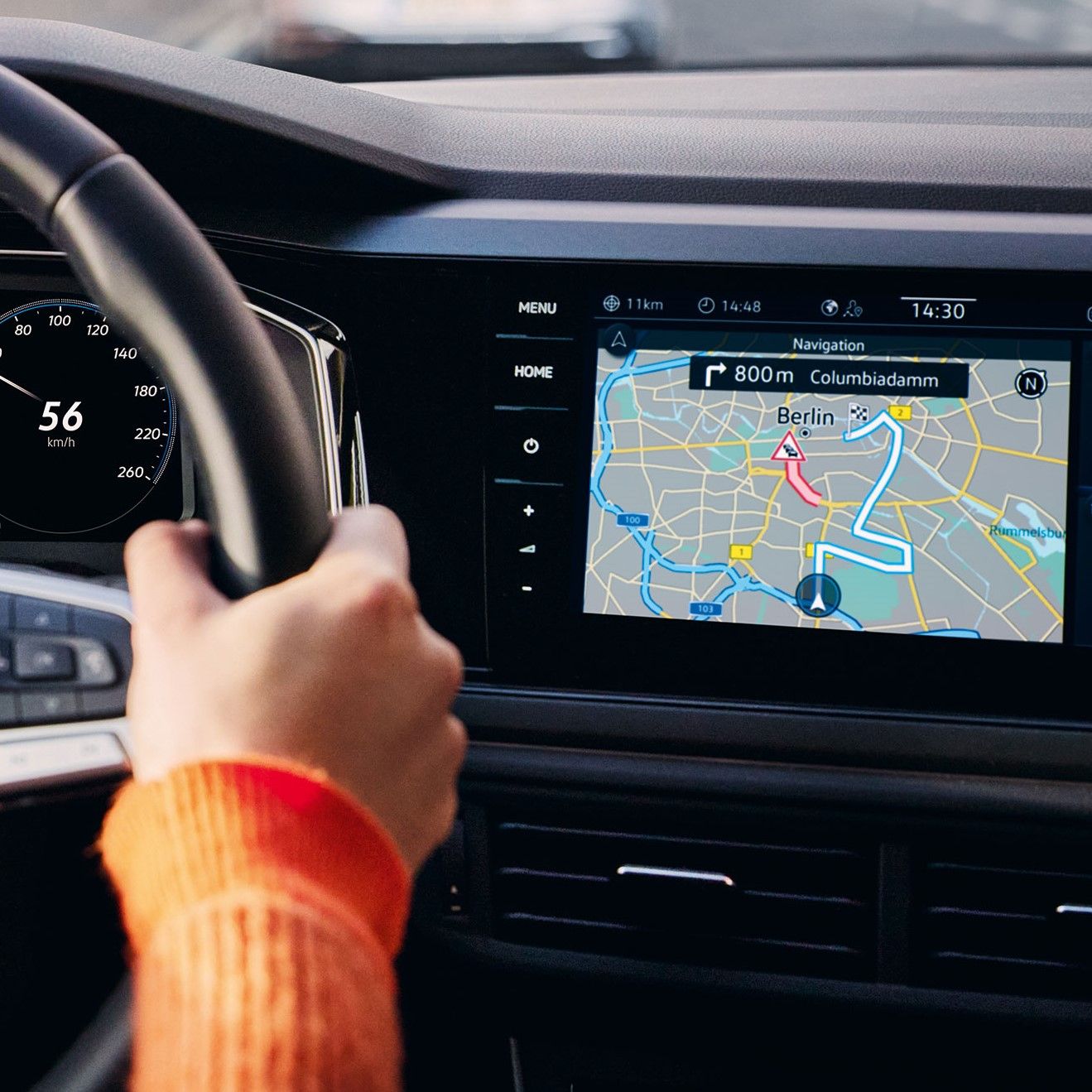 Pohľad do interiéru VW Polo s detailom na displej systému infotainment s ovládacími tlačidlami na bokoch. Na displeji je navigačná mapa. Čiastočne možno vidieť ruku, ktorá drží volant a prístrojový panel.