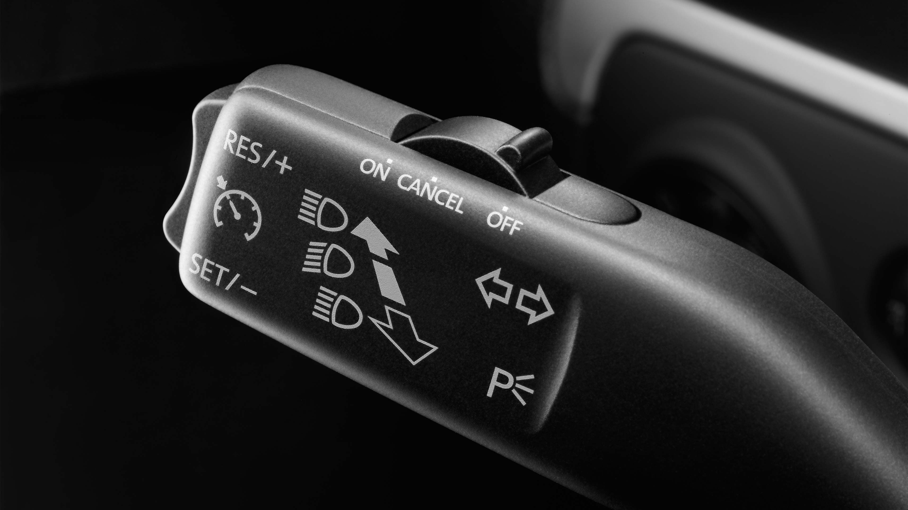 Multifunkčný prepínač v automobile. Obsahuje ovládanie tempomatu, smeroviek a parkovacích svetiel. Prepínače sú označené symbolmi a textom.