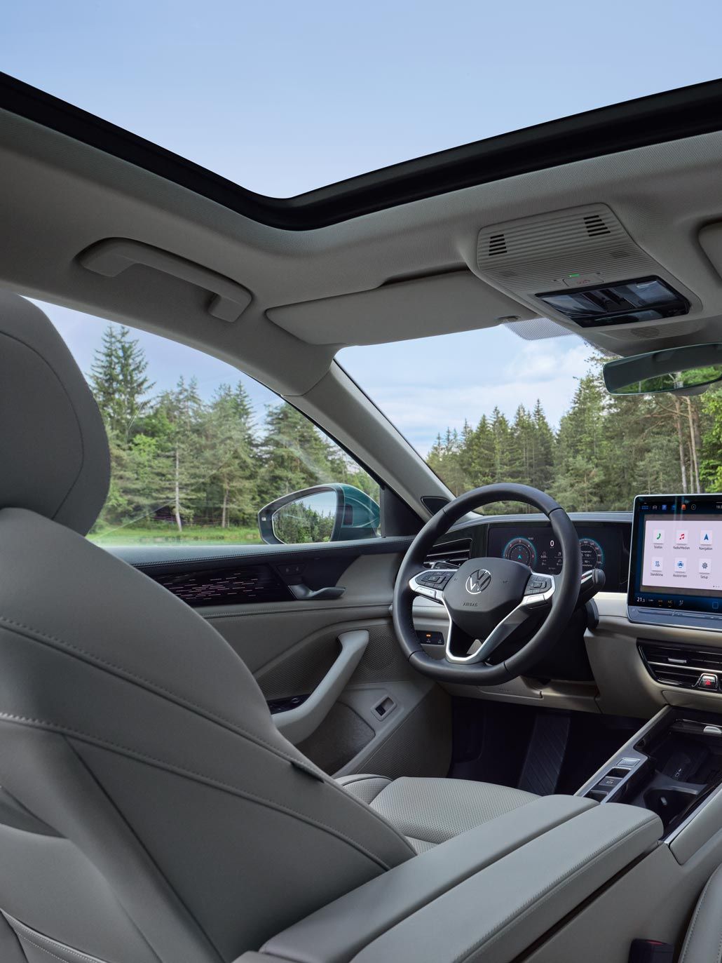 Pohľad do interiéru VW Passat s výhľadom na voliteľné sedadlá ergoActive, volant, digitálny prístrojový panel, palubnú dosku, displej systému infotainment a stredovú konzolu. Elegantný charakter mu dodáva ambientné osvetlenie. Cez čelné sklo je výhľad na les.