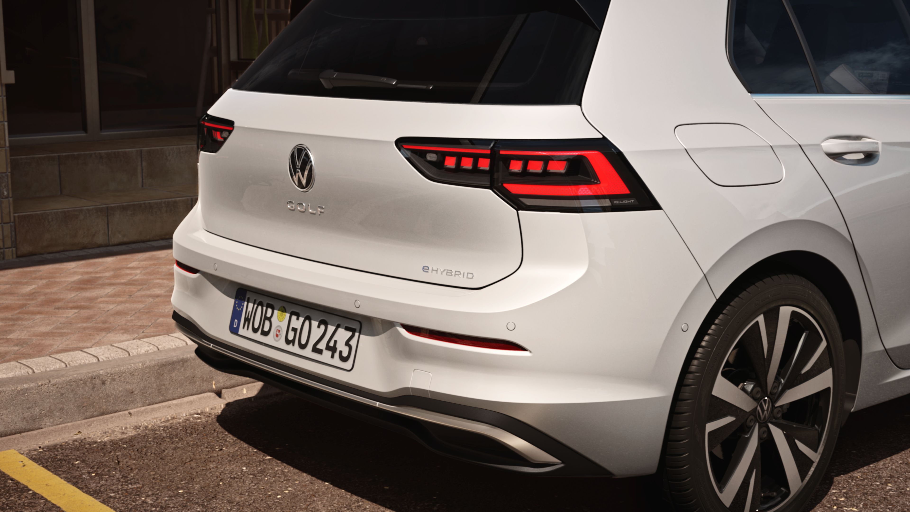 Biely Volkswagen Golf ehybrid stojí na parkovacom mieste. Obrázok sa zameriava na zadné partie vozidla s modernými zadnými LED svetlami, zadným nárazníkom logom VW a názvom modelu Golf. Na ľavej strane zadného nárazníka je umiestnený znak "eHYBRID".