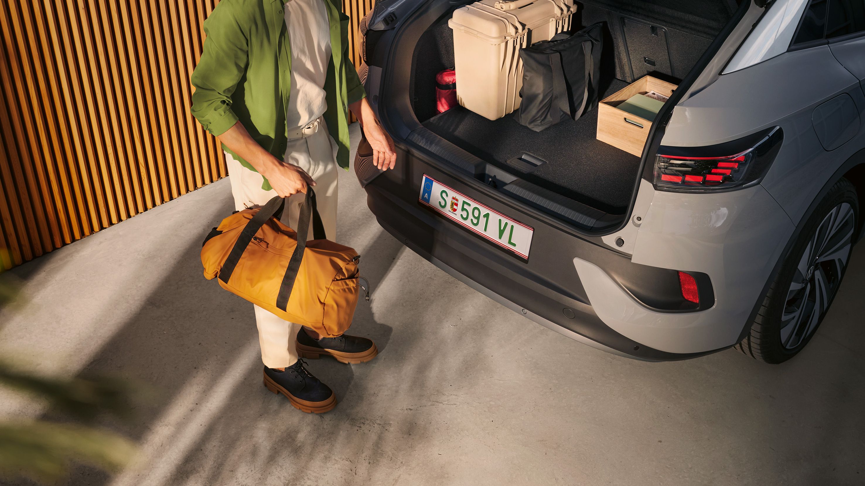 VW ID.5 s otvoreným kufrom a batožinou v ňom, pod otvorenými zadnými dverami stojí muž s taškou v ruke