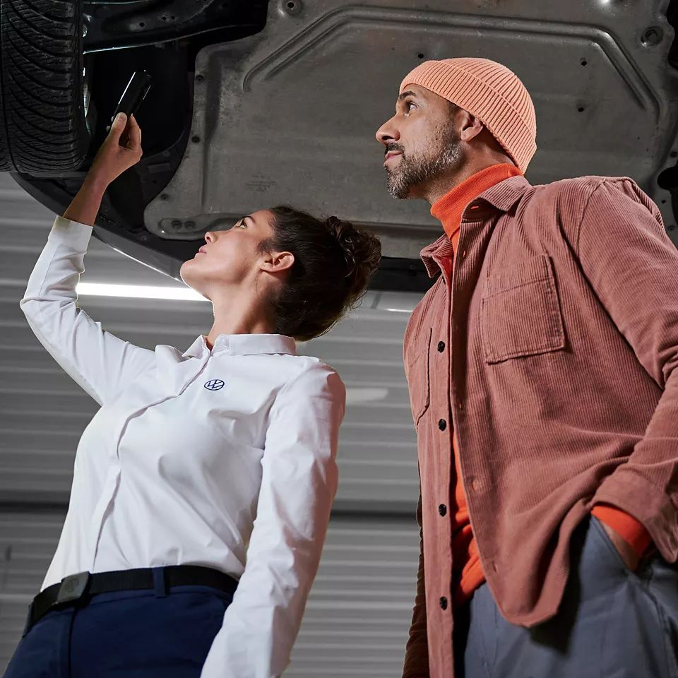 Servisná pracovníčka VW a zákazník kontrolujú podvozok vozidla VW – náhradné diely VW