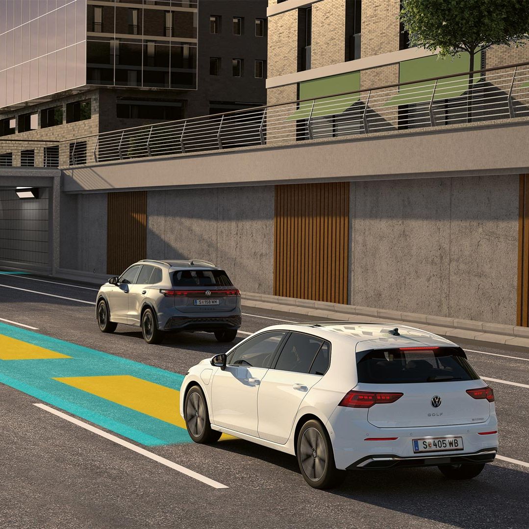 Biely VW Golf jazdí v premávke s využitím voliteľného asistenčného systému, ktorý je schematicky znázornený na obrázku. V pozadí vidieť mestské výškové budovy.