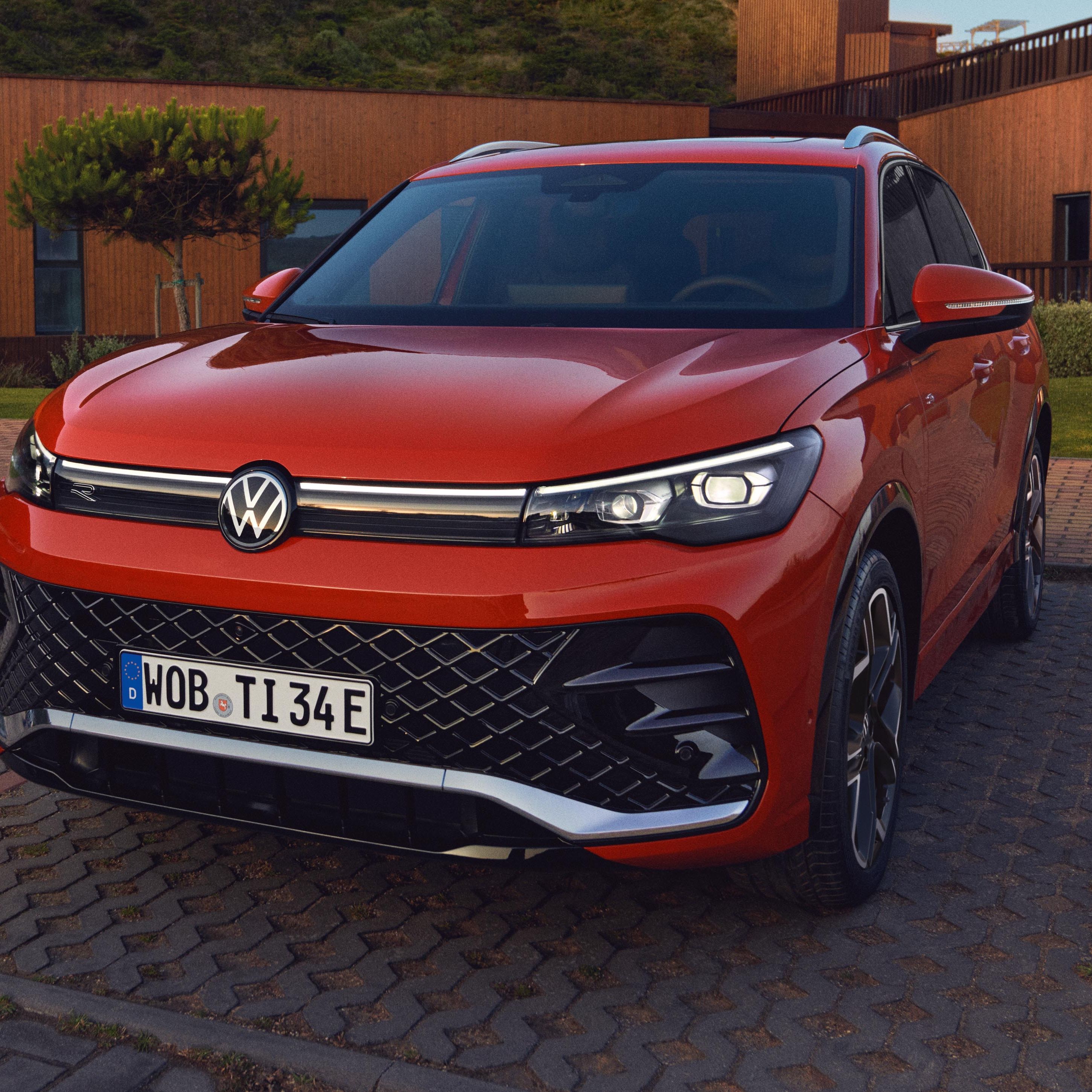 Červený VW Tiguan zaparkovaný pred veľkou, modernou, drevenou vilou s upravenou zeleňou.