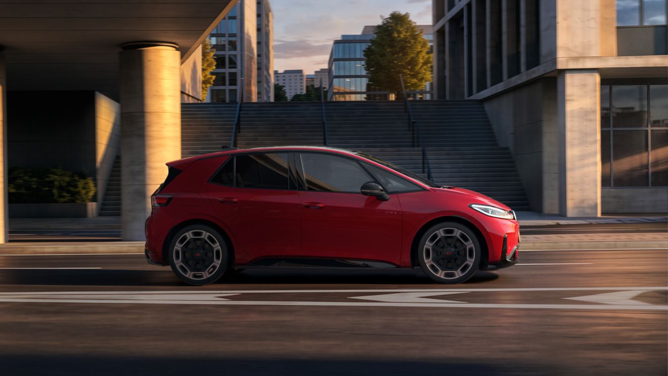 [AI-modified] – Červené VW ID.3 GTI z bočného pohľadu počas jazdy pod mostom v meste.