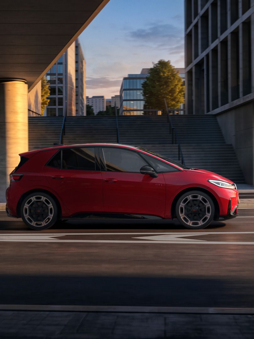 [AI-modified] – Červené VW ID.3 GTI z bočného pohľadu počas jazdy pod mostom v meste.