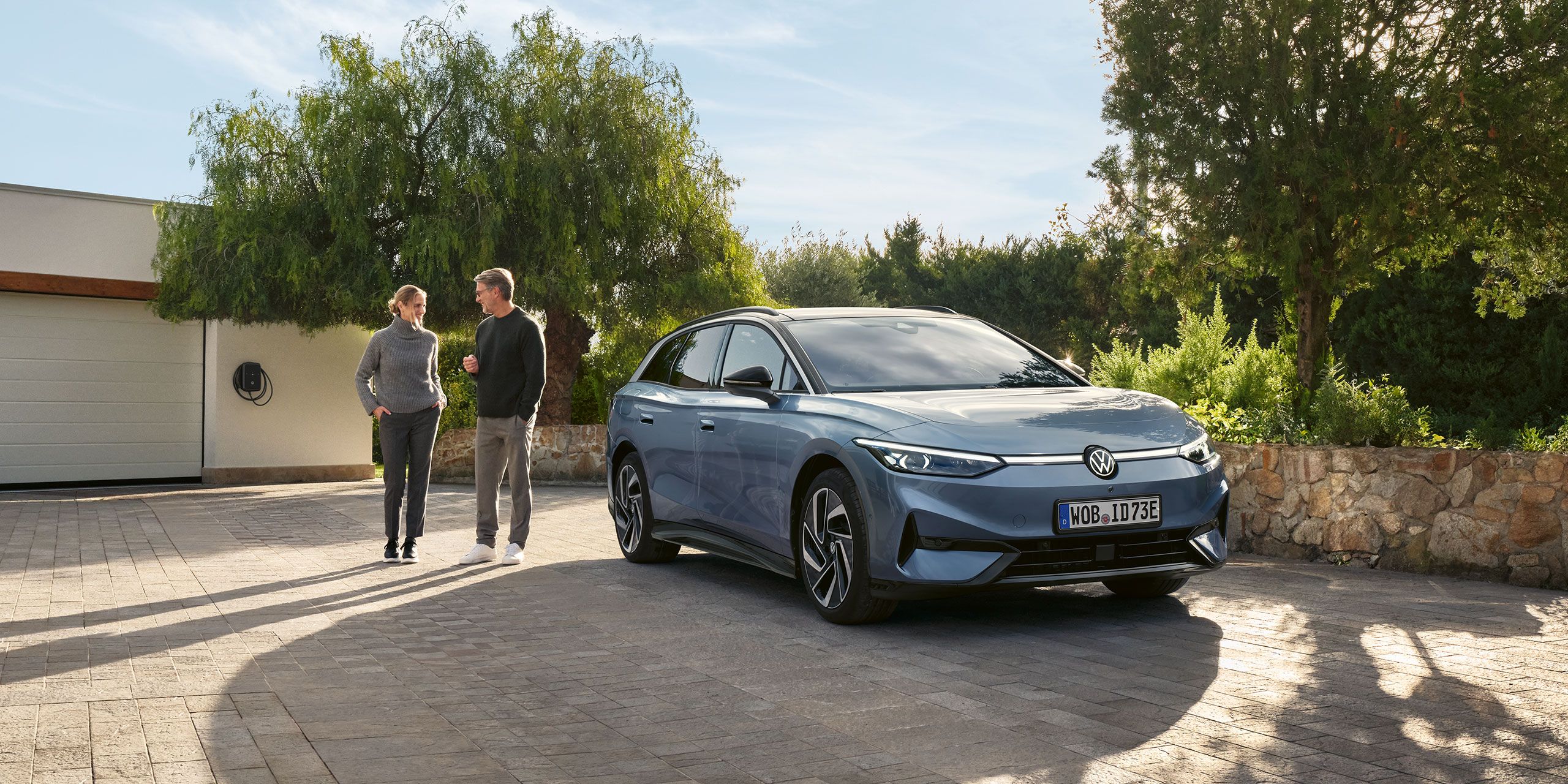 Žena a muž stojací na príjazdovej ceste vedľa svojho VW ID.7 Tourer