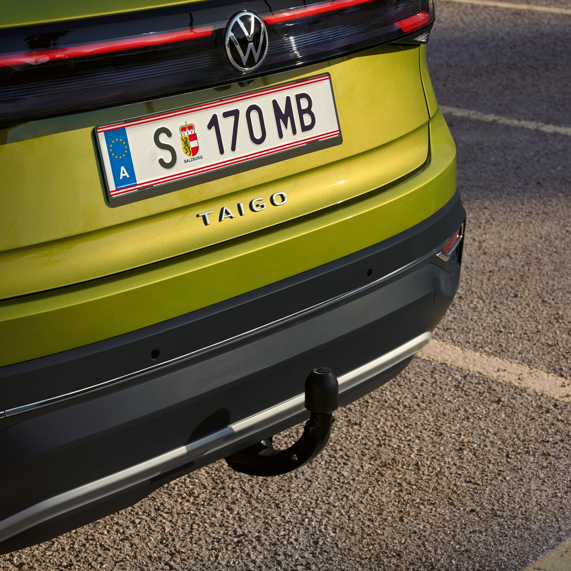 Pohľad na zadné partie zeleného VW Taigo s ťažným zariadením. Vozidlo je zaparkované na parkovacom mieste pri ceste.