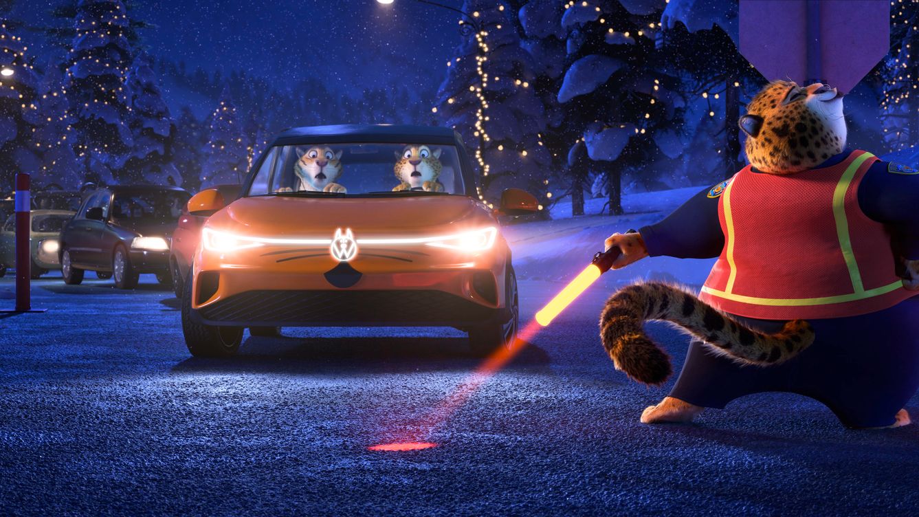 Na obrázku je zimná scenéria s vozidlami na zasneženej ceste. V popredí leopard v reflexnej veste drží svetelné tyče a riadi premávku. V žltom aute s logom VW sú dvaja tigre.