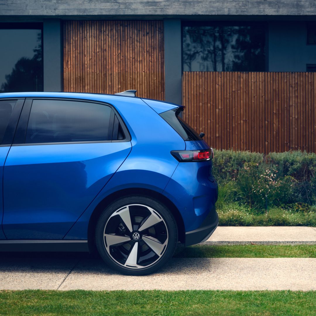 Bočný pohľad na zadnú časť modrého vozidla VW ID. Polo Style, ktoré stojí pred obytným domom so zelenou príjazdovou cestou.