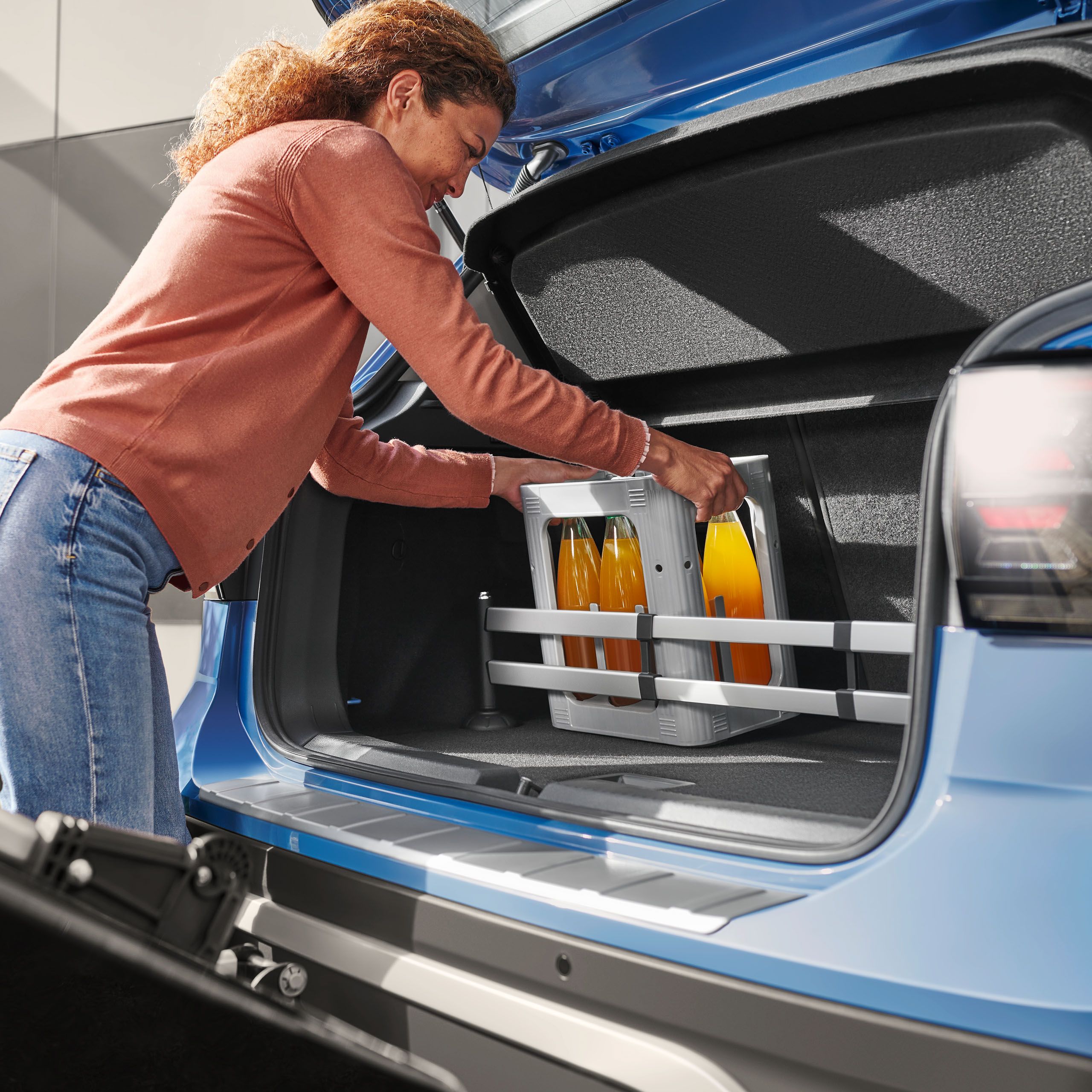 Žena nakladá do batožinového priestoru produkty, zásuvný modul do batožinového priestoru od VW Accessories upevňuje prepravku na nápoje