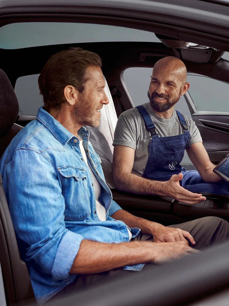 Zákazník sedí v aute, servisný technik VW mu niečo vysvetľuje na tablete.