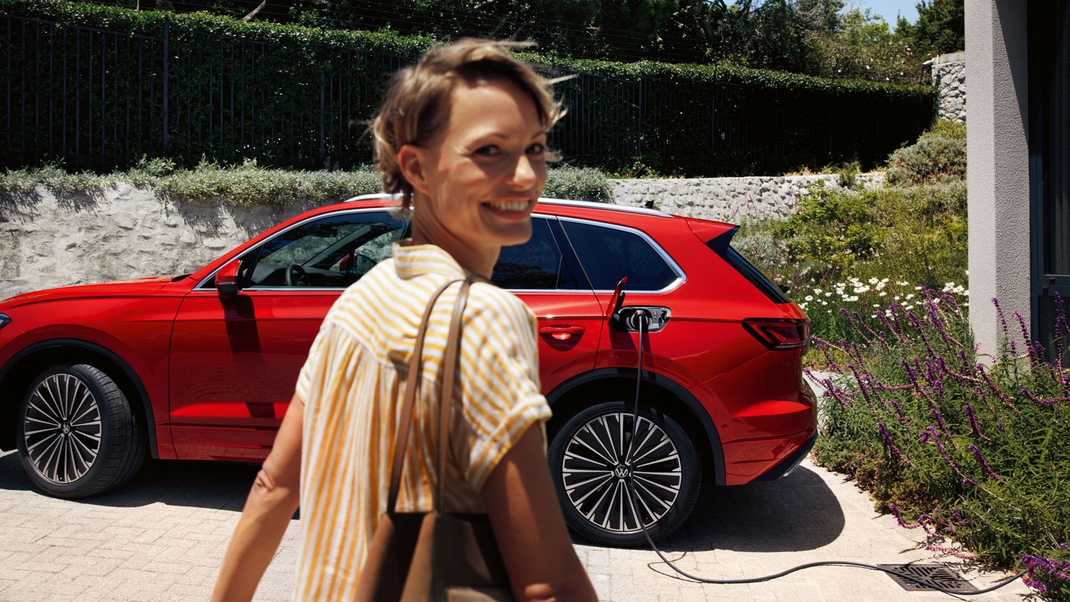 V popredí usmiatá žena, v pozadí sa nabíja VW Touareg Elegance eHybrid.