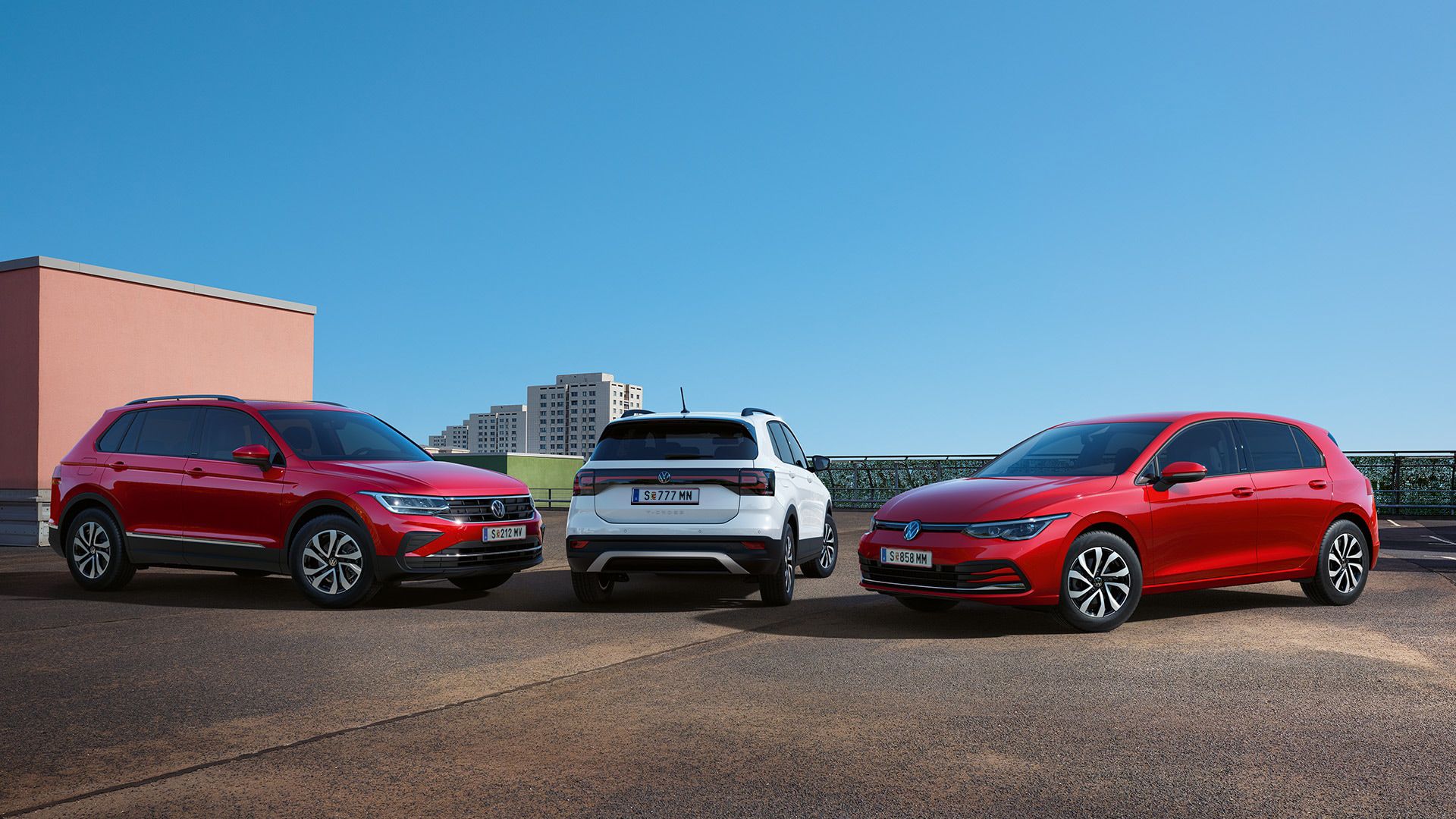 VW T-Cross, VW Golf a VW Tiguan stoja vedľa seba na streche parkovacieho domu. V pozadí vidieť bytovky a modrú oblohu..