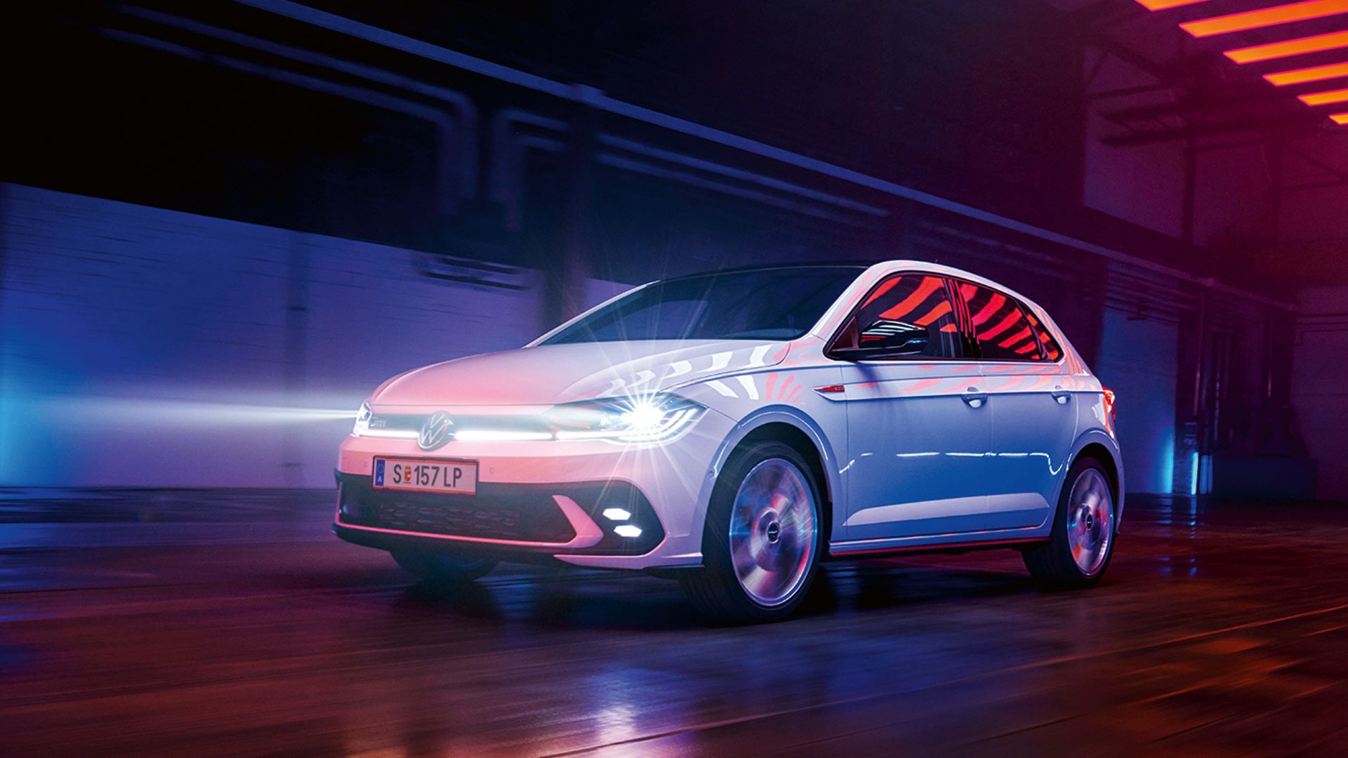 Biely VW Polo GTI jazdí v hale so zapnutými Matrix LED svetlometmi a svetelným pásom vpredu.
