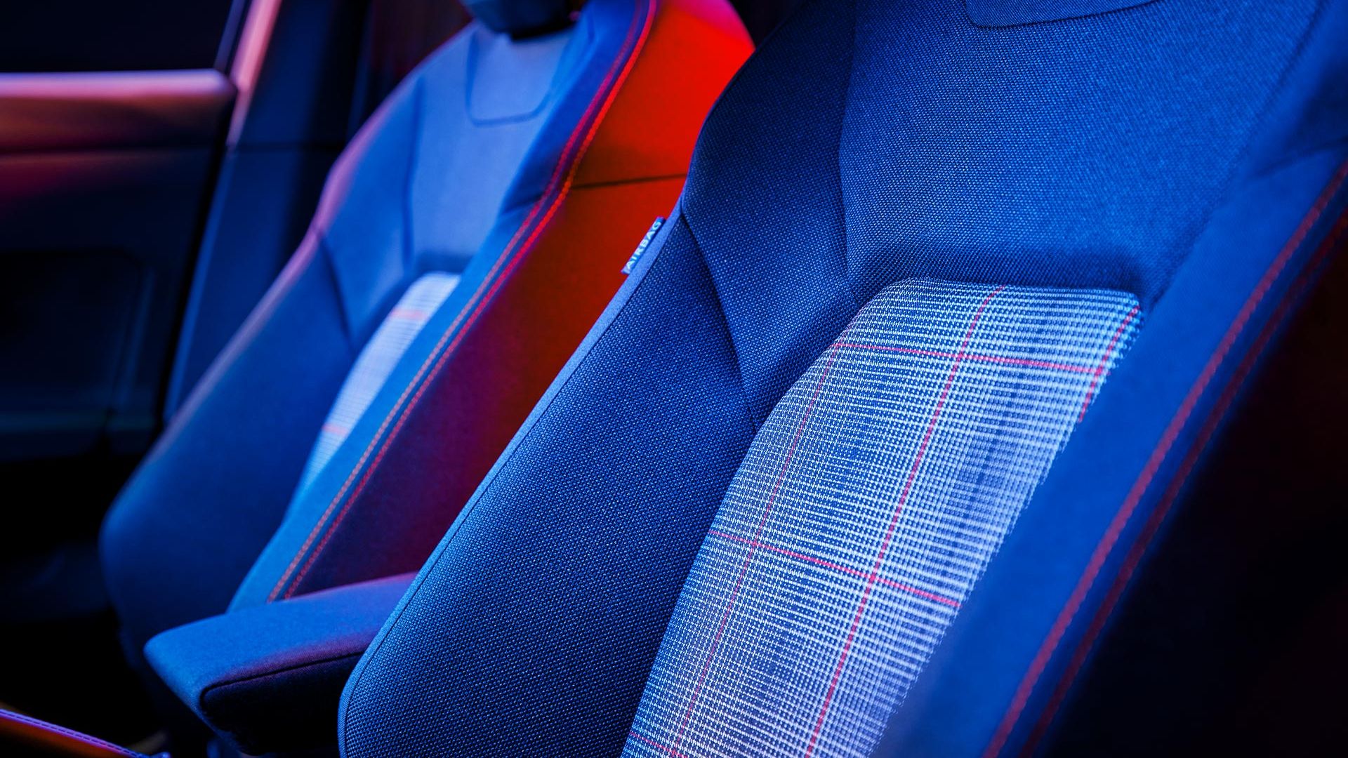 Interiér automobilu so zameraním na predné sedadlá nasvietené  modrým a červeným osvetlením. Sedadlá sú ergonomické s moderným dizajnom a kontrastnými textúrami.