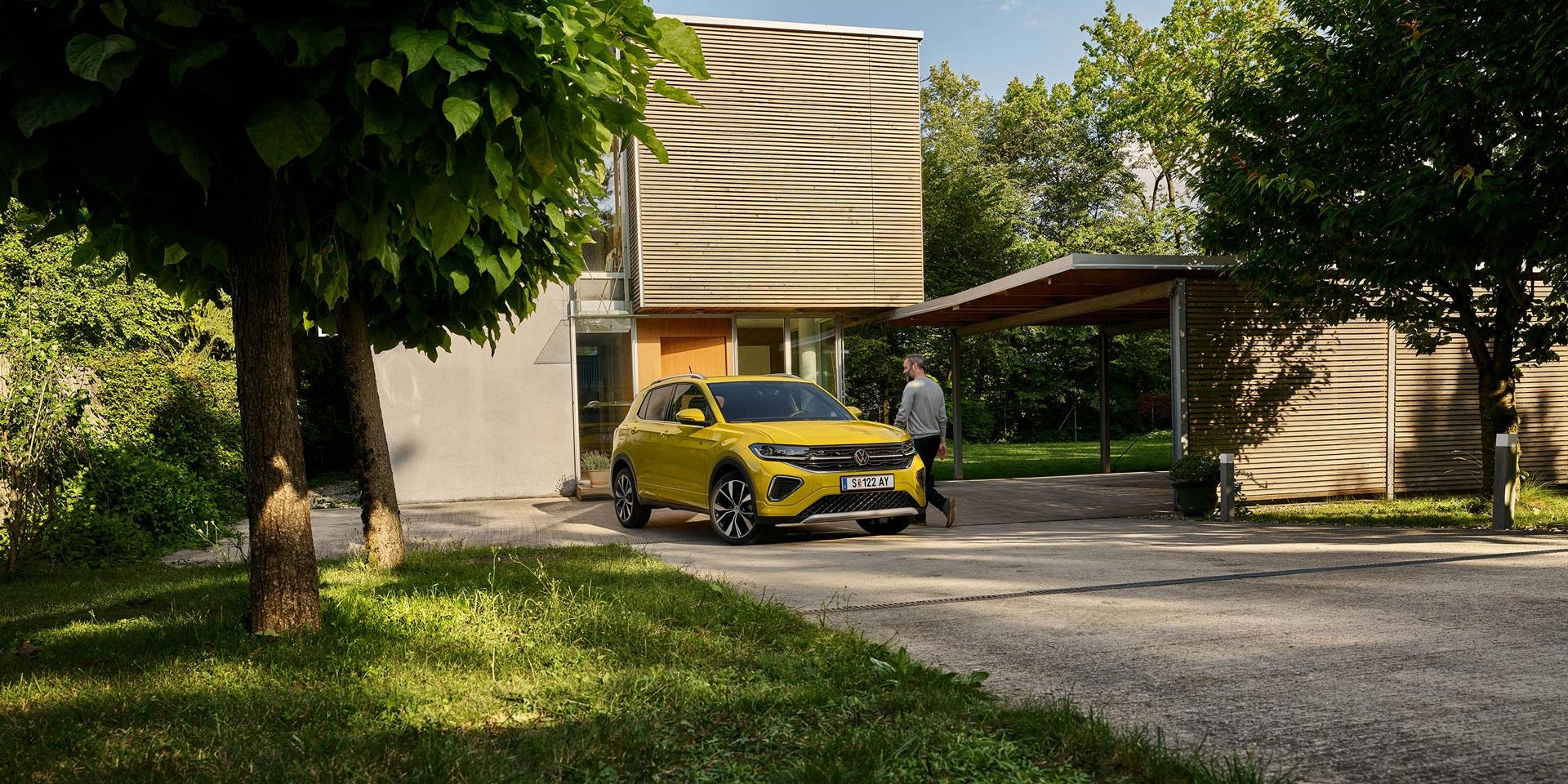 Muž sa chystá nastúpiť do žltého VW T-Cross, ktoré je zaparkované na príjazdovej ceste k domu.