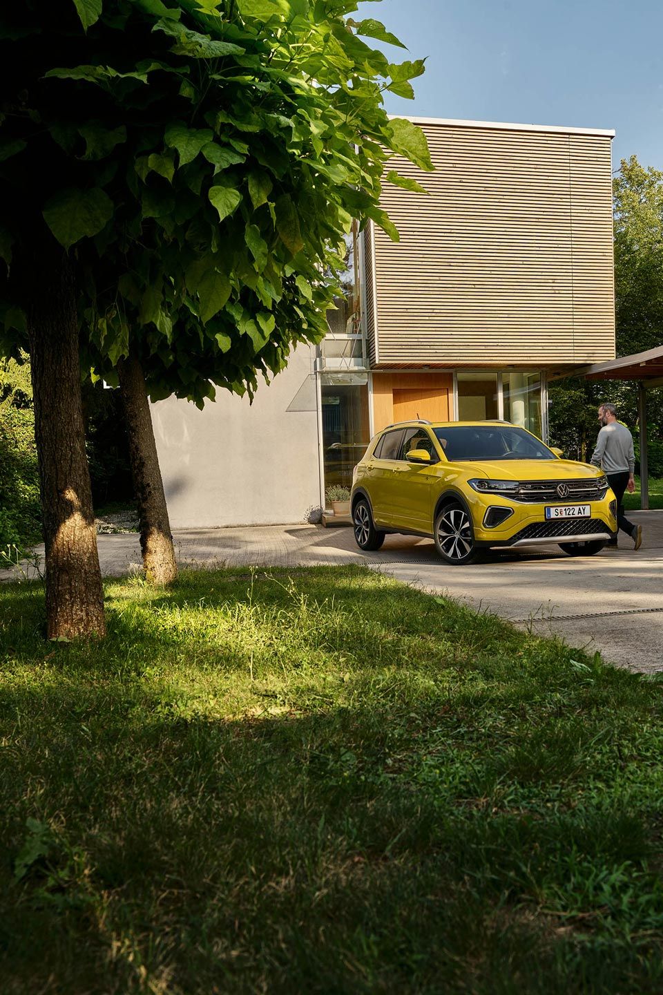 Muž sa chystá nastúpiť do žltého VW T-Cross, ktoré je zaparkované na príjazdovej ceste k domu.