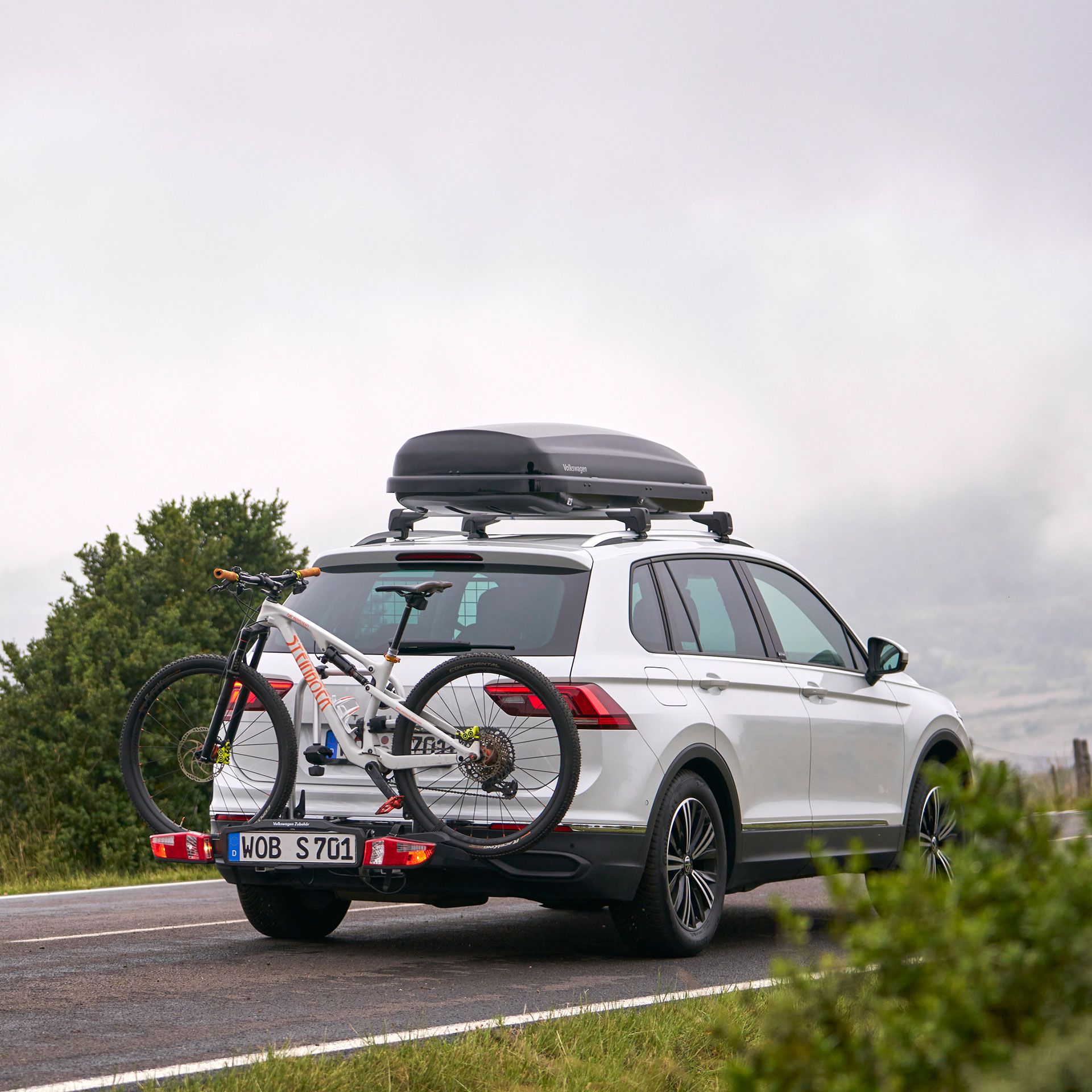 VW Tiguan so strešným boxom a nosičom bicyklov z originálneho príslušenstva Volkswagen vrátane bicykla na poľnej ceste