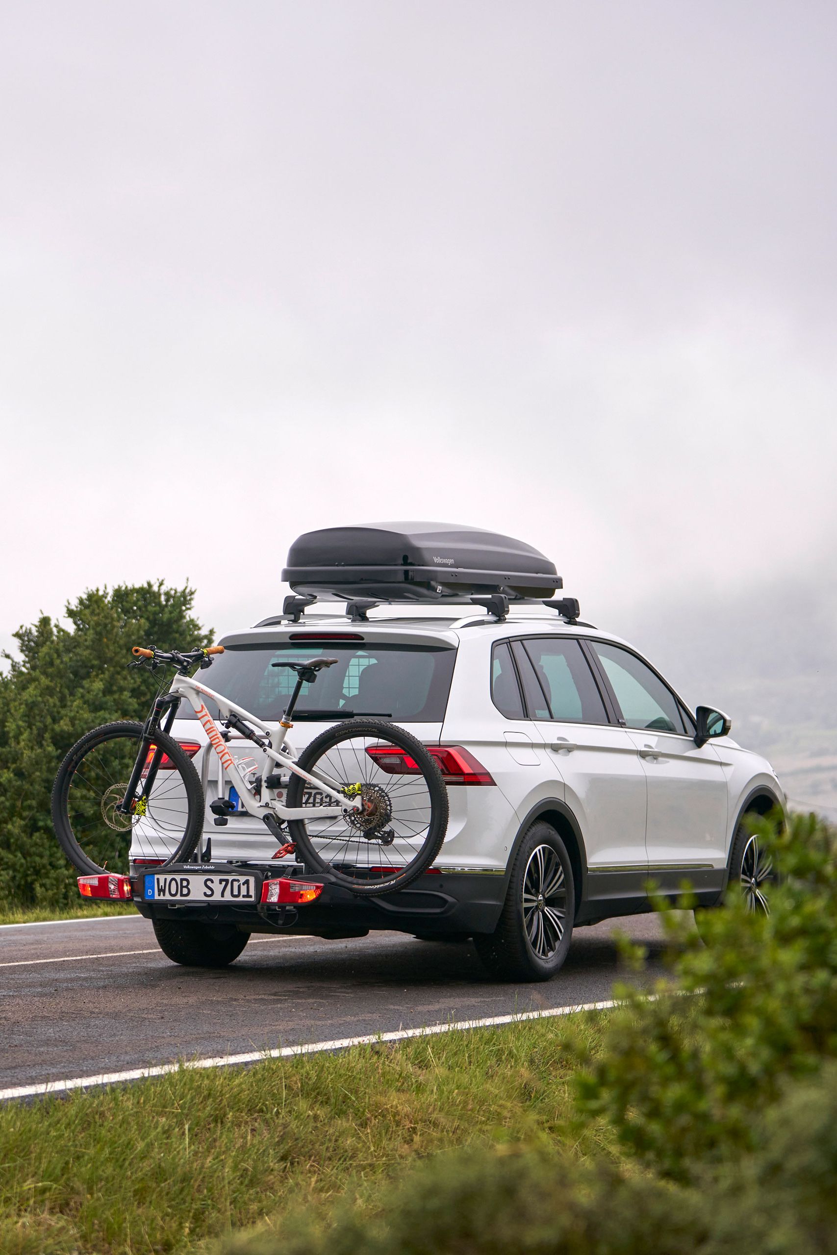 VW Tiguan so strešným boxom a nosičom bicyklov z originálneho príslušenstva Volkswagen vrátane bicykla na poľnej ceste
