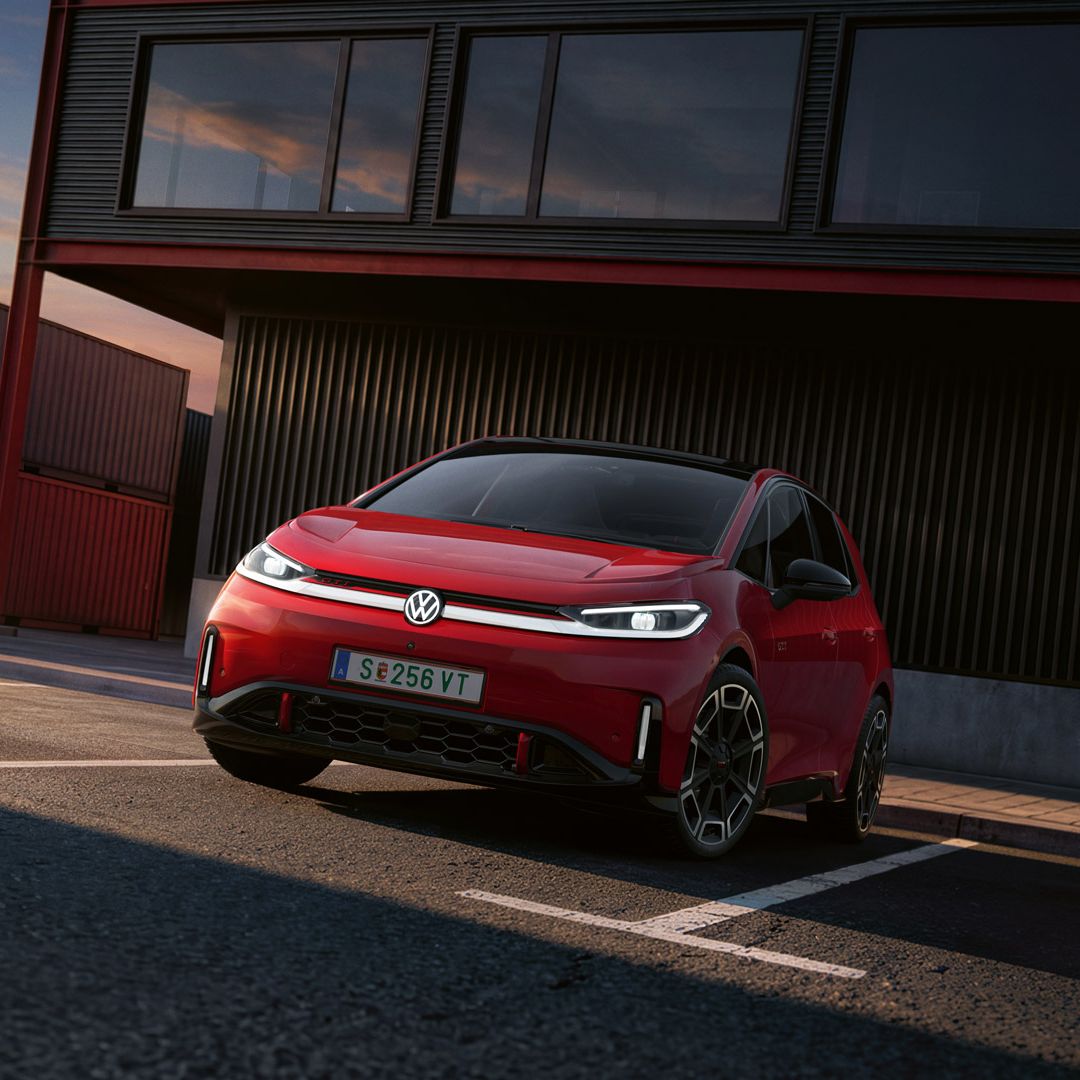 [AI-modified] – Pohľad na predné partie červené VW ID.3 GTI so zapnutými svetlami a rozsvieteným logom pred budovou.