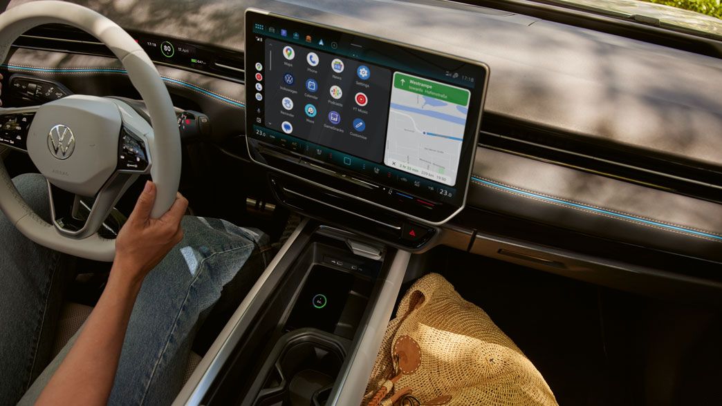 Pohľad do interiéru vozidla. na mieste vodiča sedí žena a drží volant. Na displeji systému infotainment je navigačná a ikony funkcií vozidla. Dobre vidieť aj otvorenú stredovú konzolu. Pod sedadlom spolujazdca má položenú nákupnú tašku.
