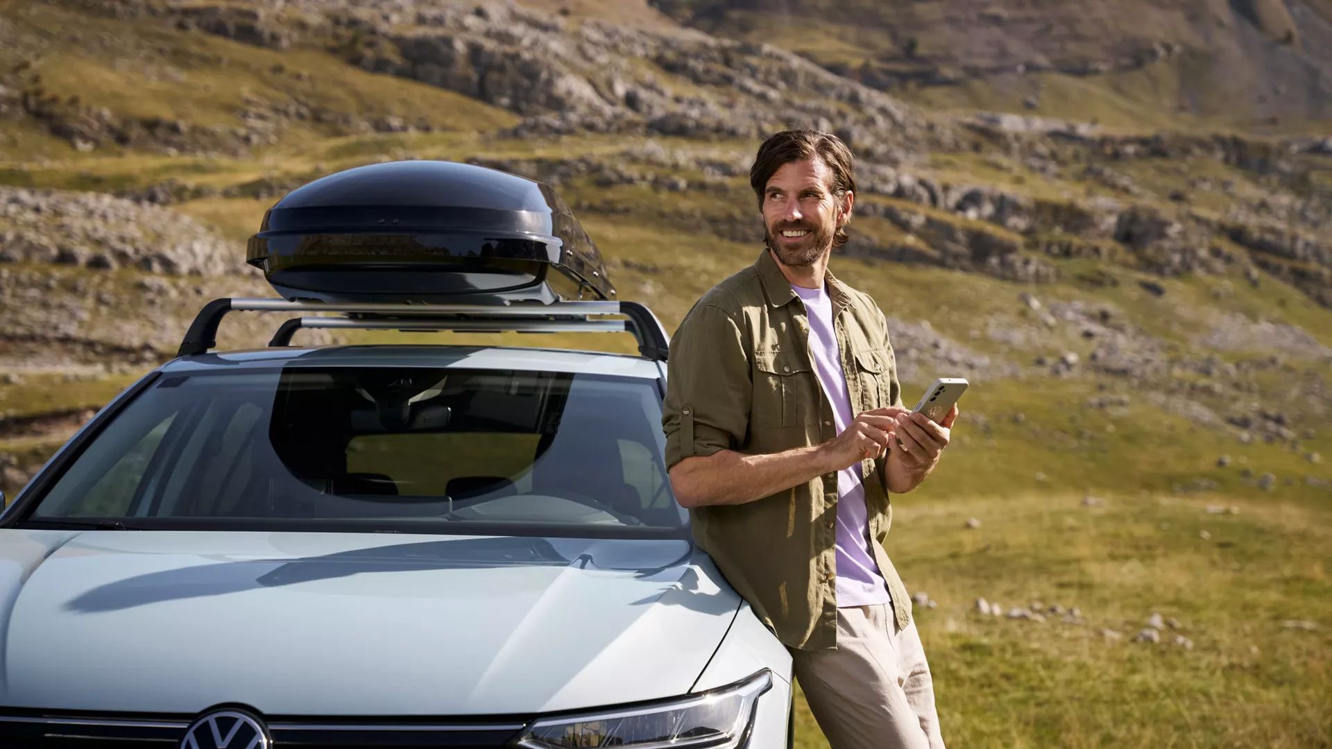 Muž so smartfónom opretý o auto VW s príslušenstvom strešný box